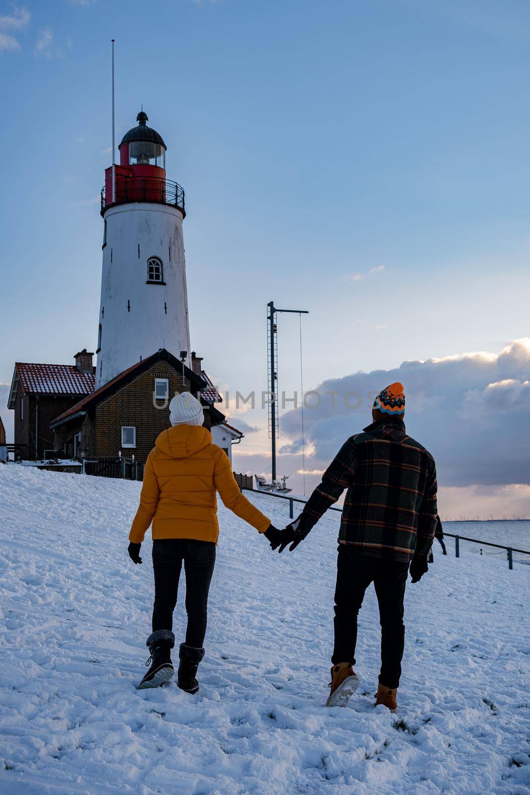 couple men and woman by the lighthouse of Urk Netherlands during winter in the snow by fokkebok