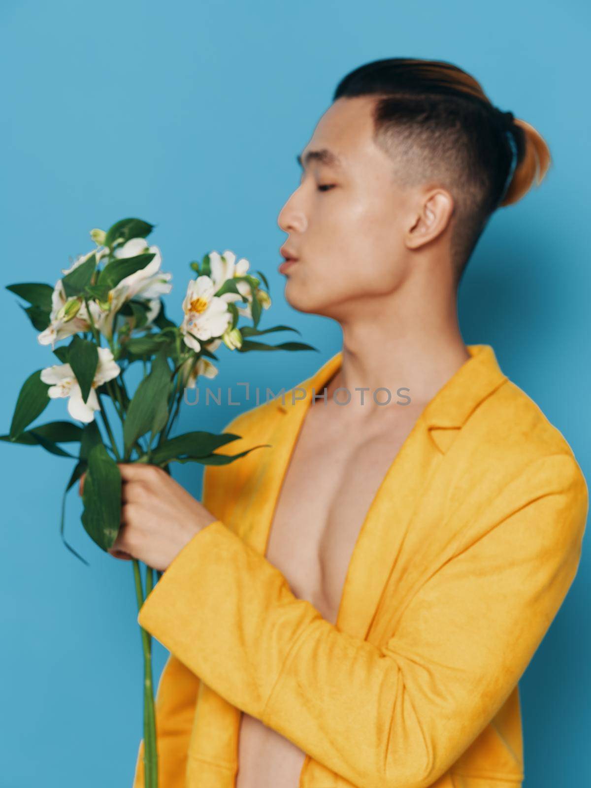 Nice guy with a bouquet of white flowers on a blue background in a yellow coat. High quality photo