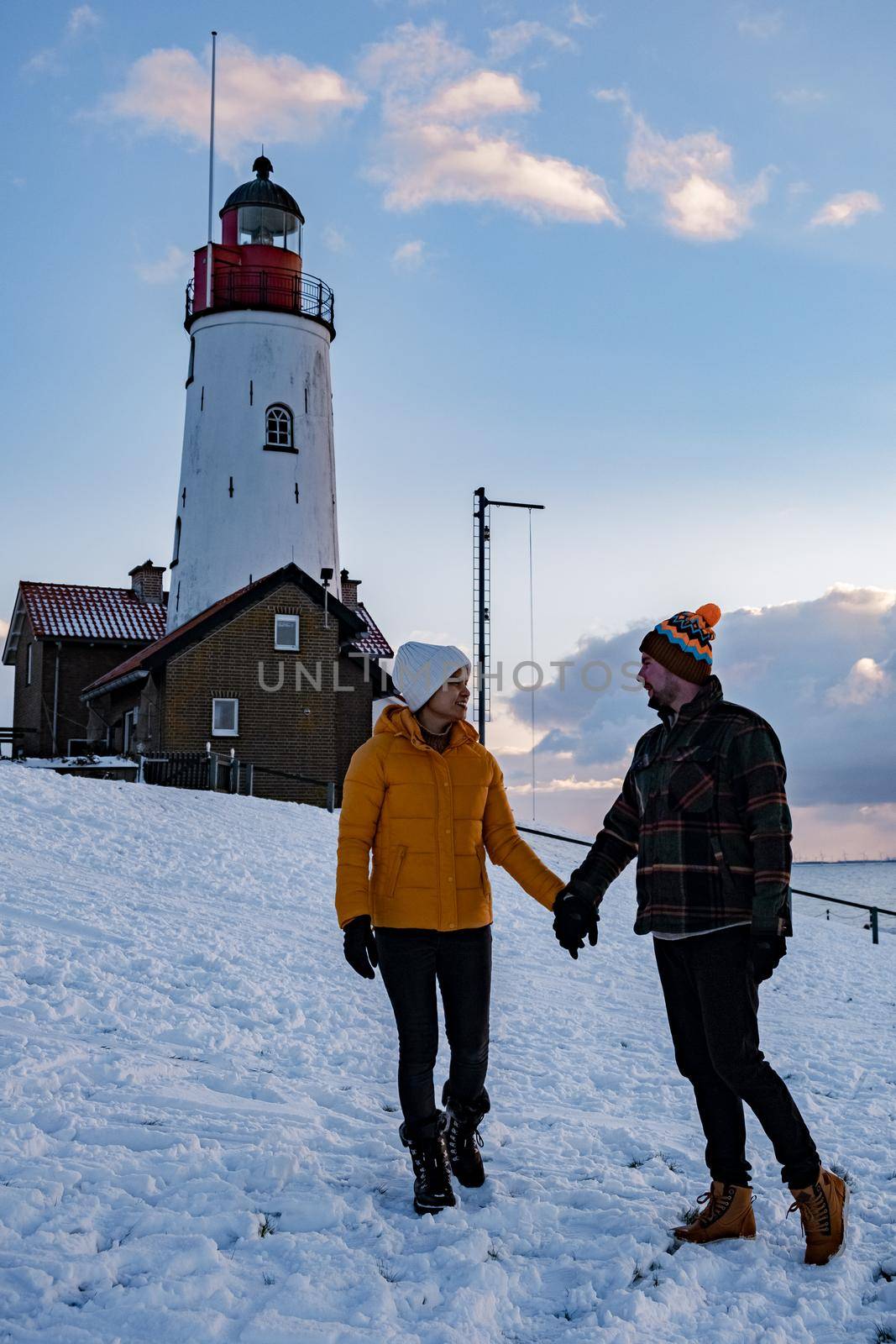 couple men and woman by the lighthouse of Urk Netherlands during winter in the snow by fokkebok