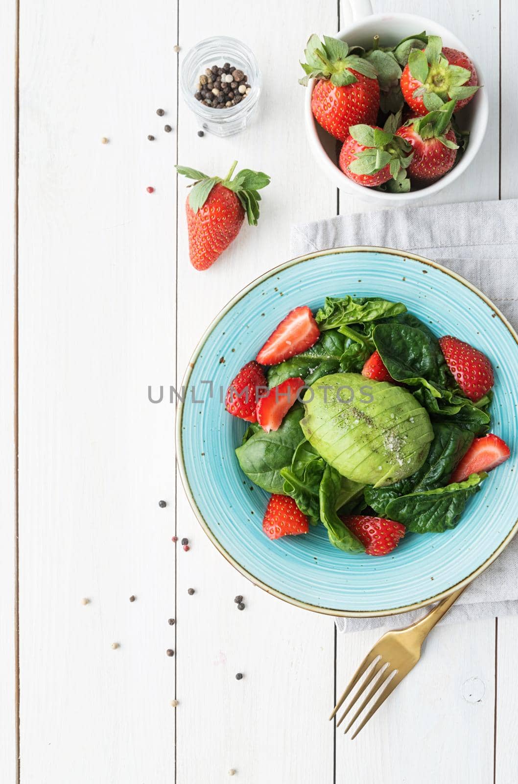 Salad with strawberries, avocados, spinach on a white wooden background top view flat lay by Desperada