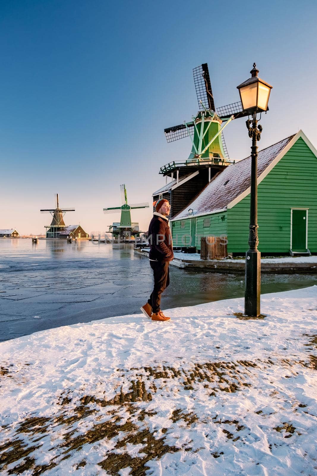 young man walked in the snow, snow covered windmill village in the Zaanse Schans Netherlands, historical wooden windmills in winter Zaanse Schans Holland during winter