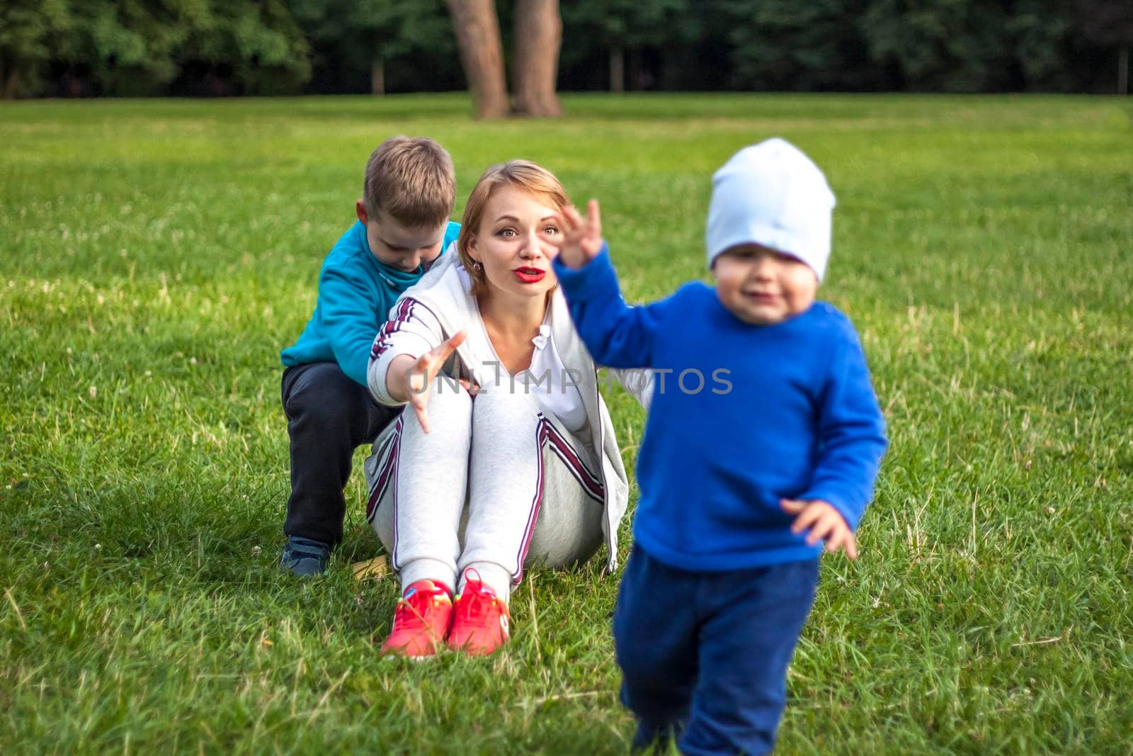 A girl plays with her sons on a green lawn. Live emotions of mother and son. by Alina_Lebed