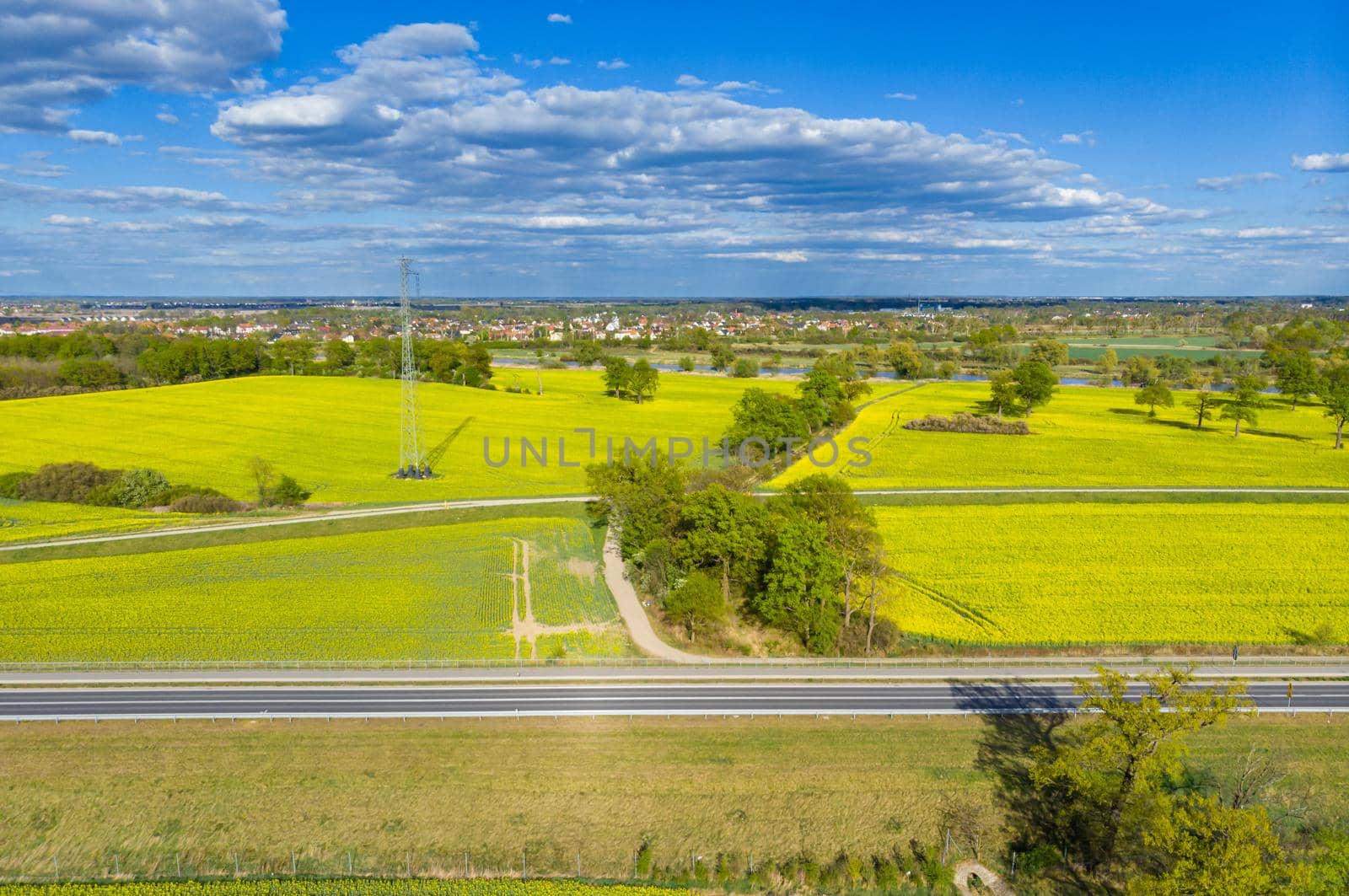 Aerial drone look to long highway between yellow fields of colza at cloudy sunny day