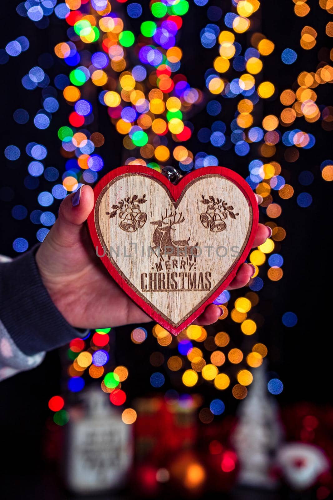 Holding Christmas heart shape decoration isolated on background with blurred lights. December season, Christmas composition. by vladispas