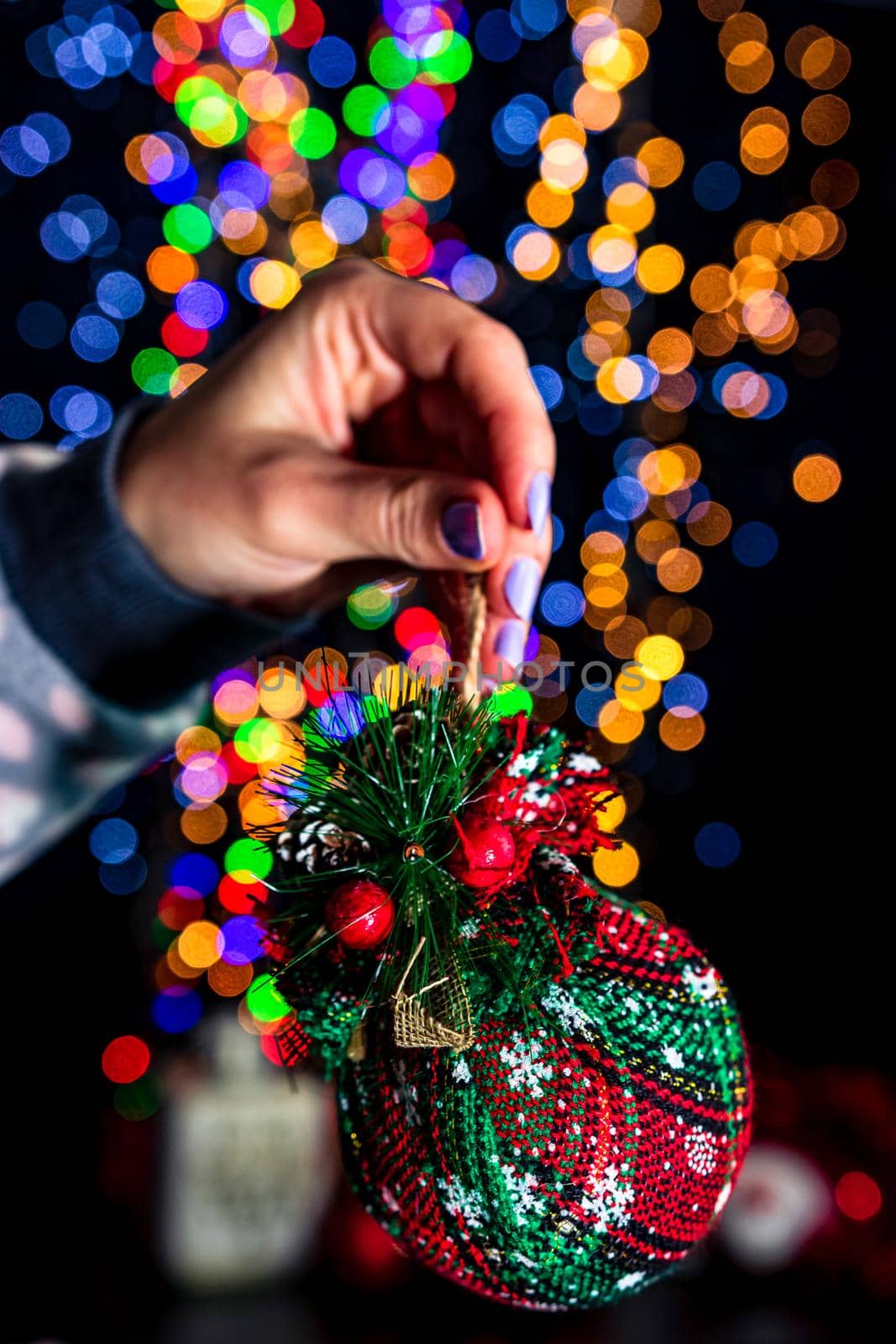 Holding Christmas bauble decoration isolated on background with blurred lights. December season, Christmas composition.
