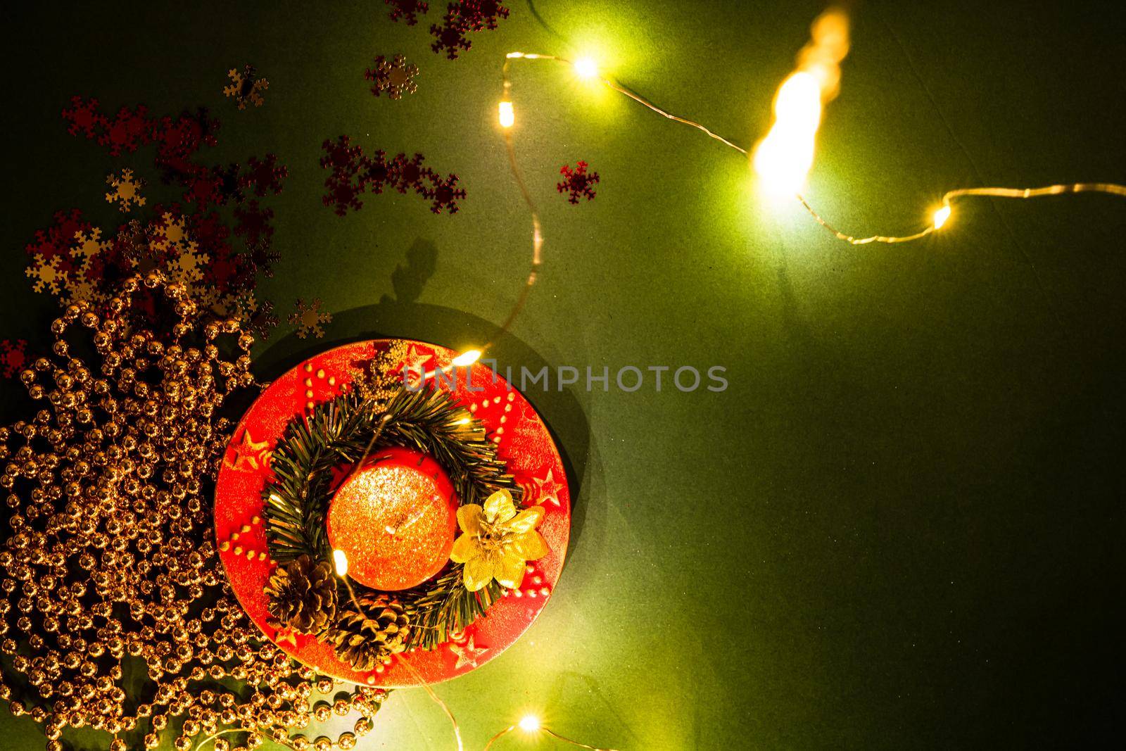 Christmas lights over a december season composition with ornaments and decorations. Top view with copy space on green background.