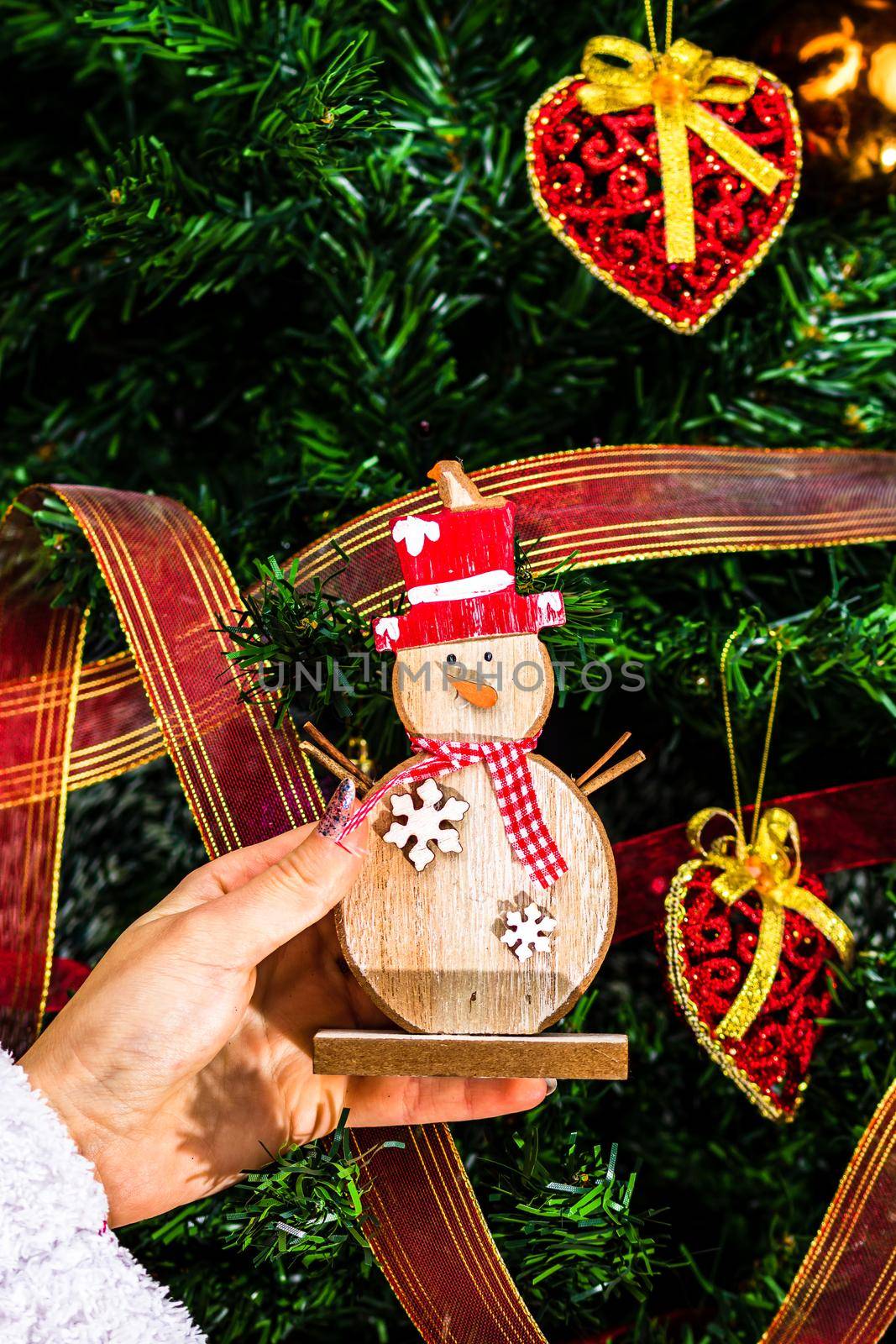 Hands holding Christmas snowman figurine in front of the Christmas tree. Decorating the fir tree isolated by vladispas