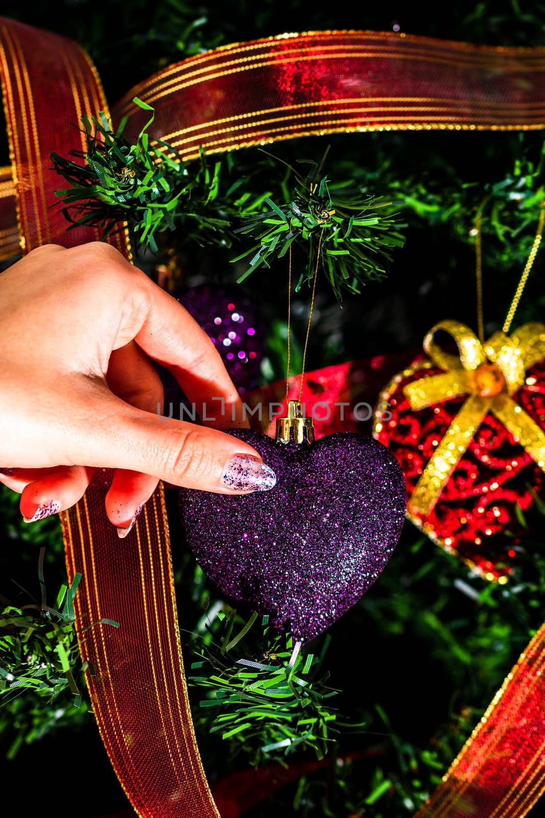 Hand putting heart shaped Christmas decorations on fir branches decorating Christmas tree, Christmas hanging decorations. by vladispas
