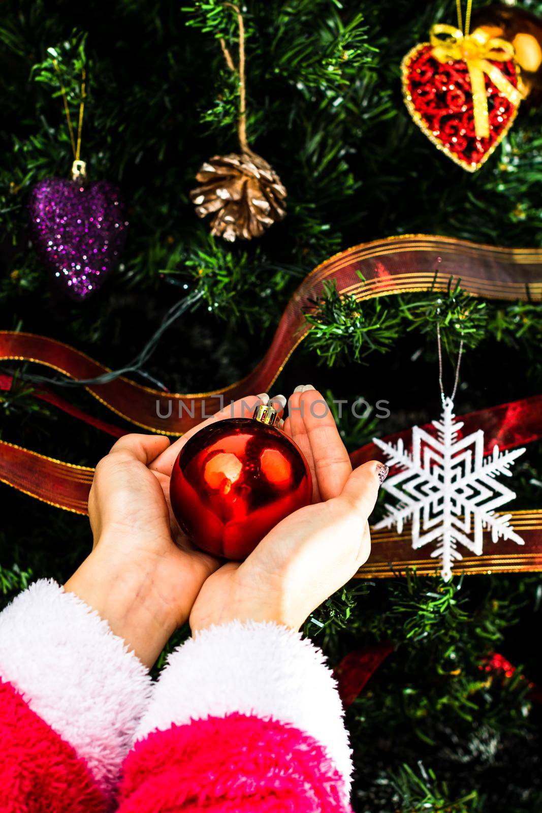 Hands holding Christmas ornament in front of Christmas tree. Decorating fir branches with Christmas decorations. by vladispas
