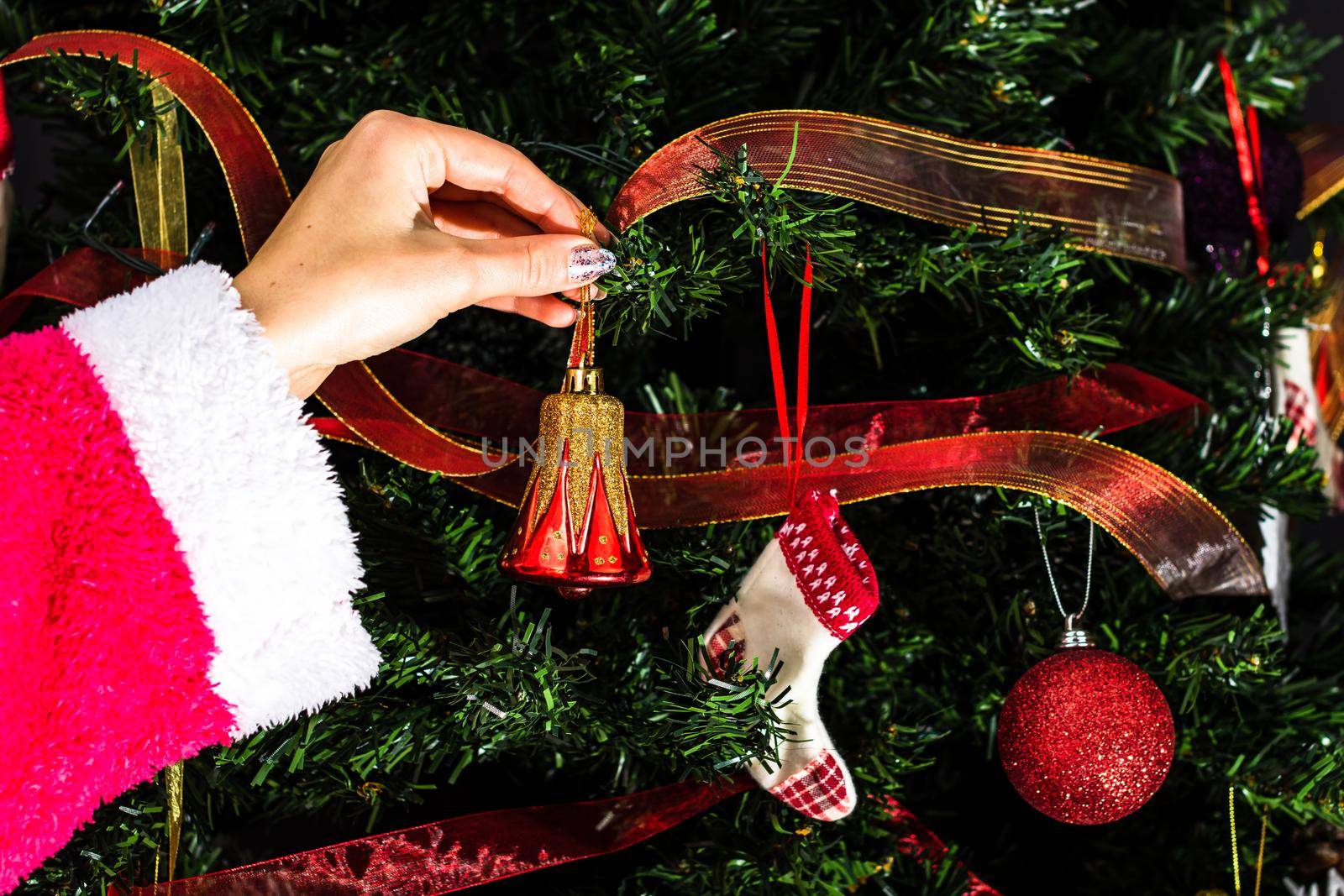 Decorating Christmas tree, hand putting Christmas decorations on fir branches. Christmas hanging decorations.