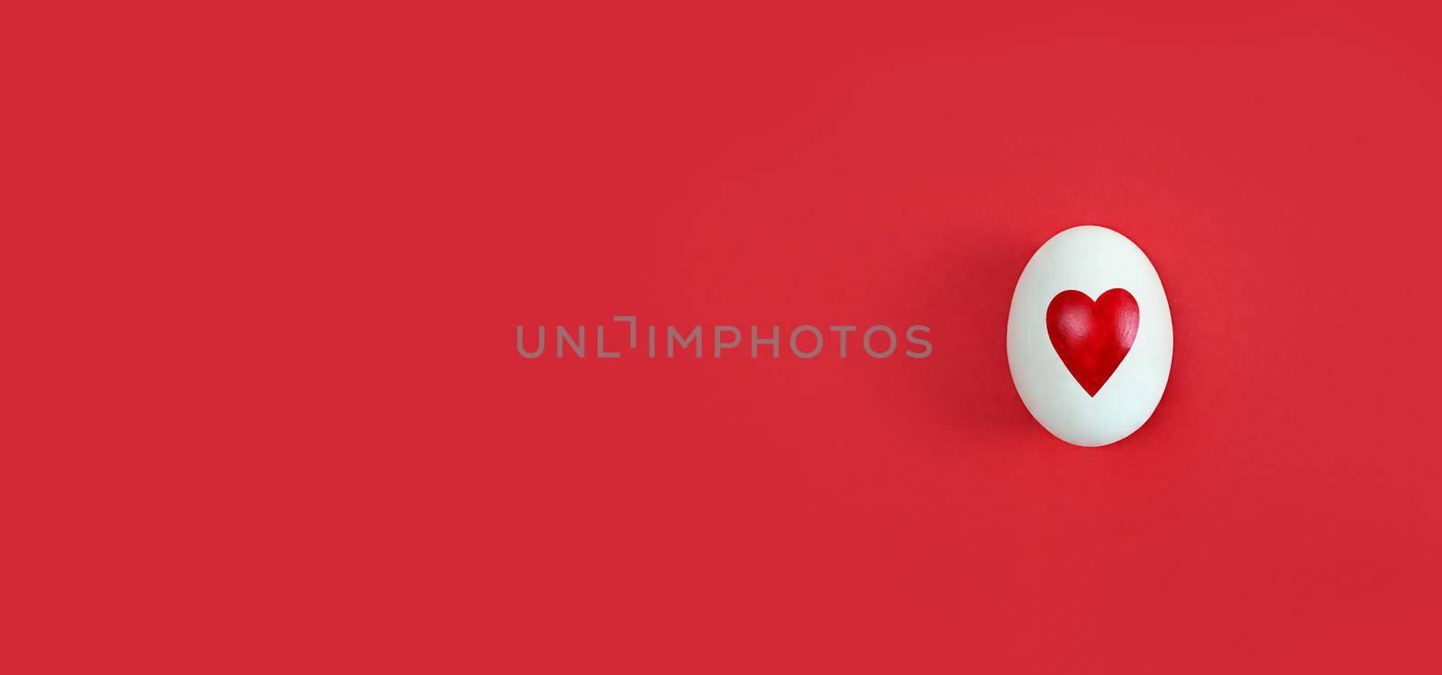 White egg with heart shape on a red background with copy space.