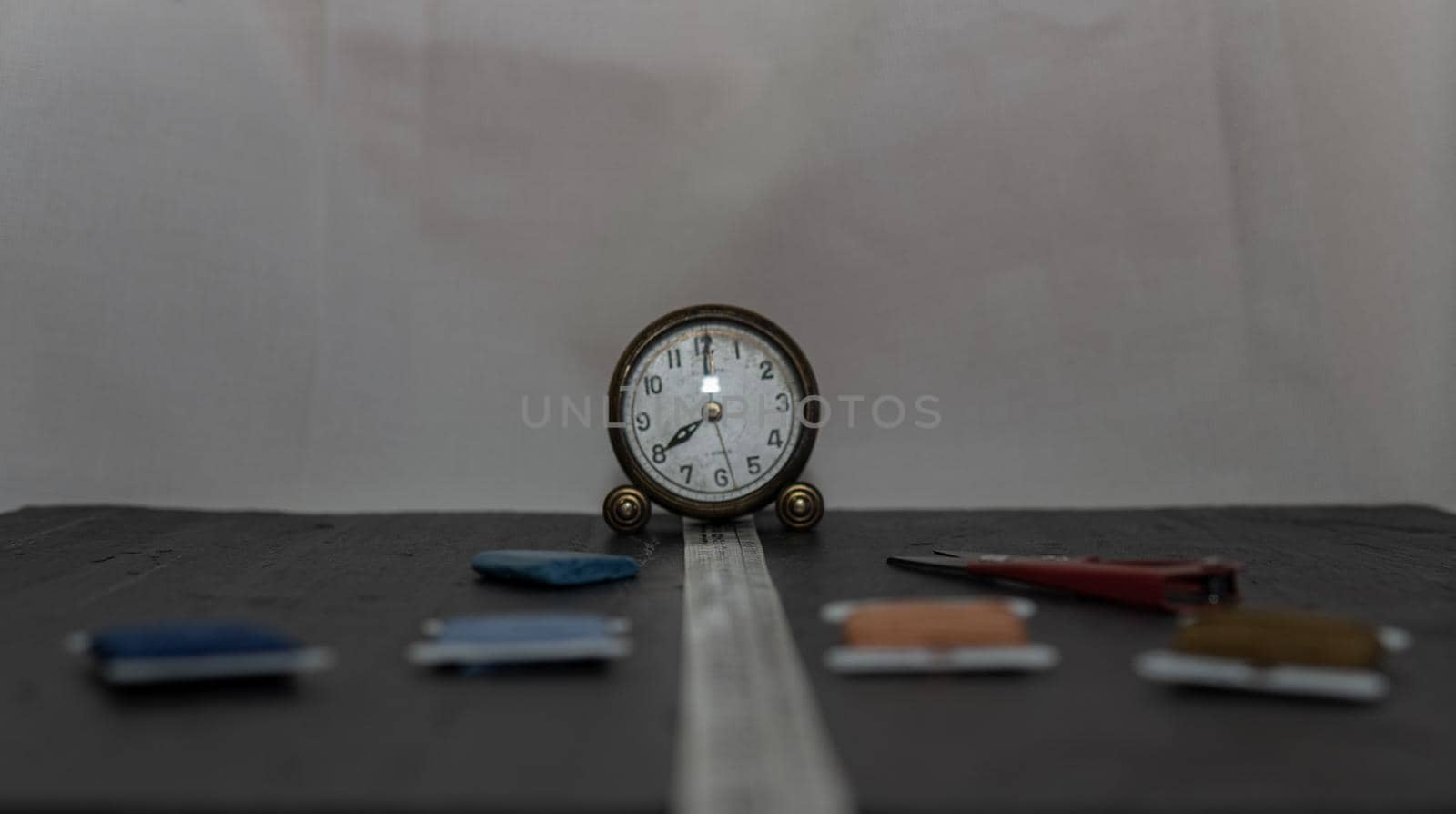 Clock surrounded by sewing utensils such as needle, thread and sewing tape measure. by xavier_photo