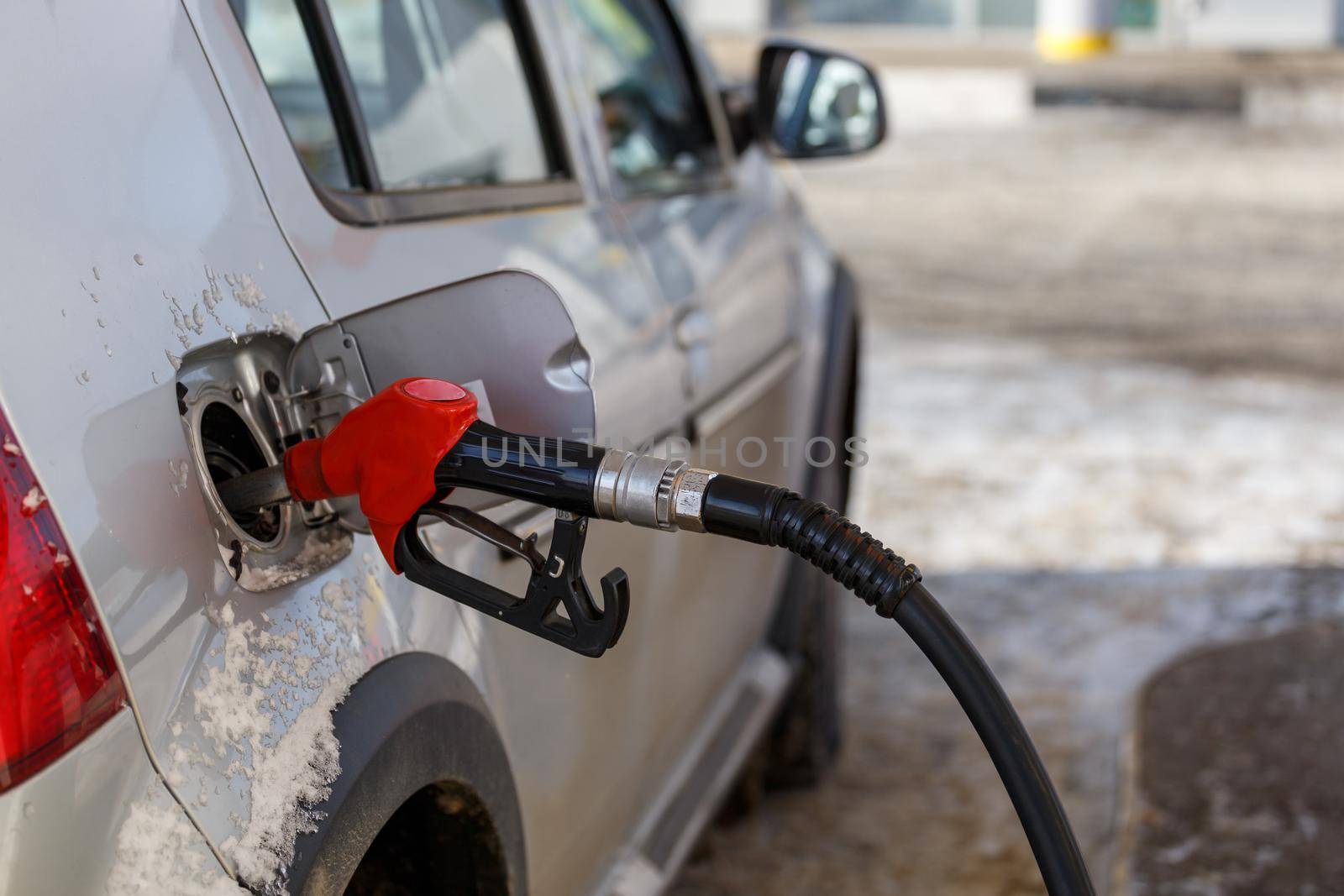 silver metallic car refueling on winter day gas station - close-up with selective focus and blurry background.