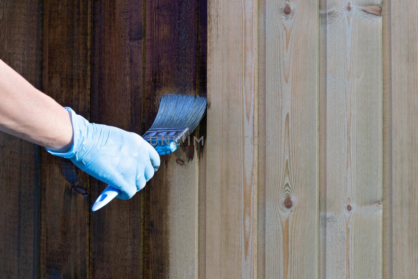 Painting a wooden wall with brown paint with a brush.