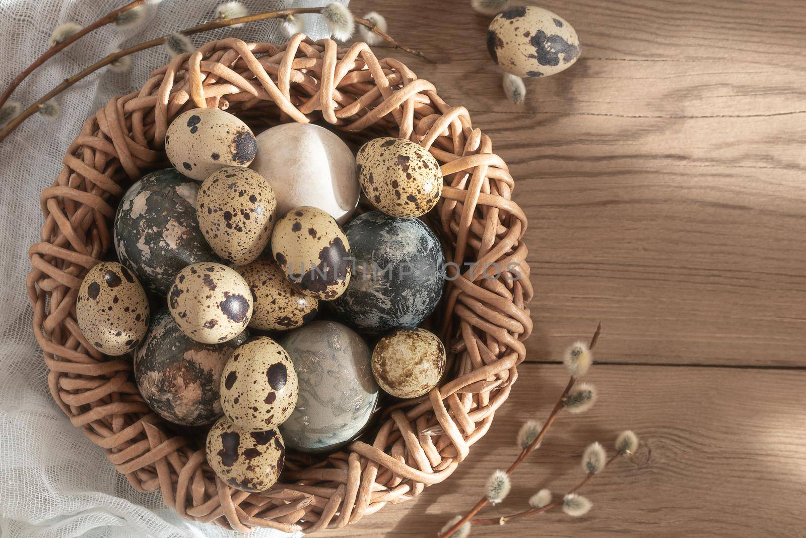 Easter composition - Easter eggs painted with natural dyes in a wicker nest on a wooden table, copyspace by galsand