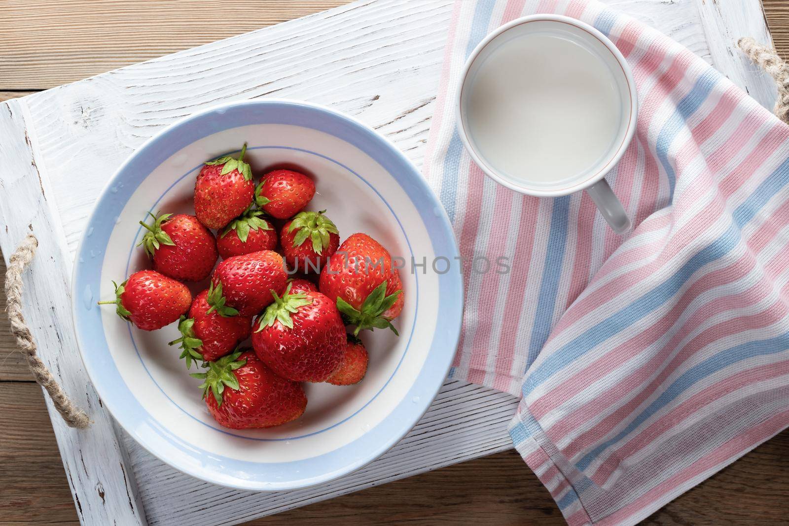Natural ripe strawberries in a white bowl and milk in a mug on a white wooden tray. Top view by galsand