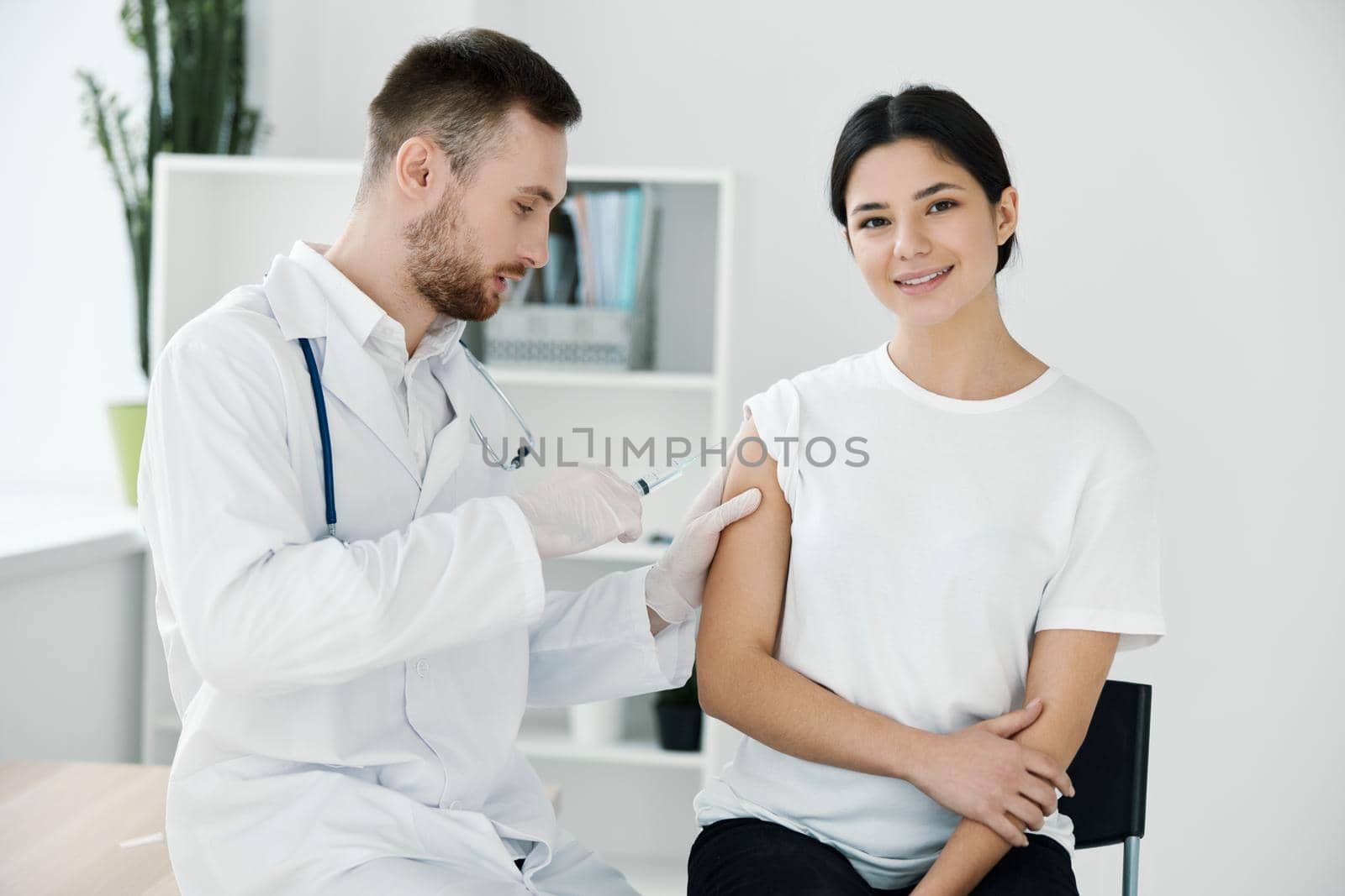 the doctor injects the covid-19 vaccine into the shoulder of the patient in a white t-shirt on a light background by SHOTPRIME