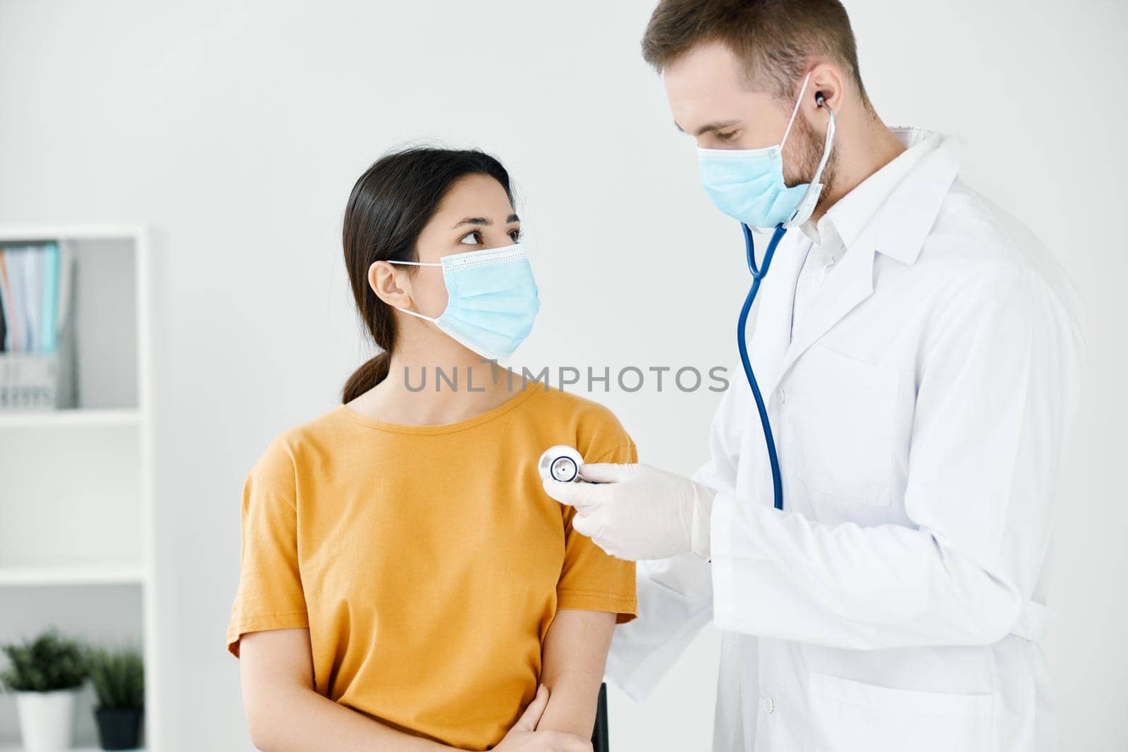 doctor in medical mask and coat examining woman in yellow t-shirt by SHOTPRIME