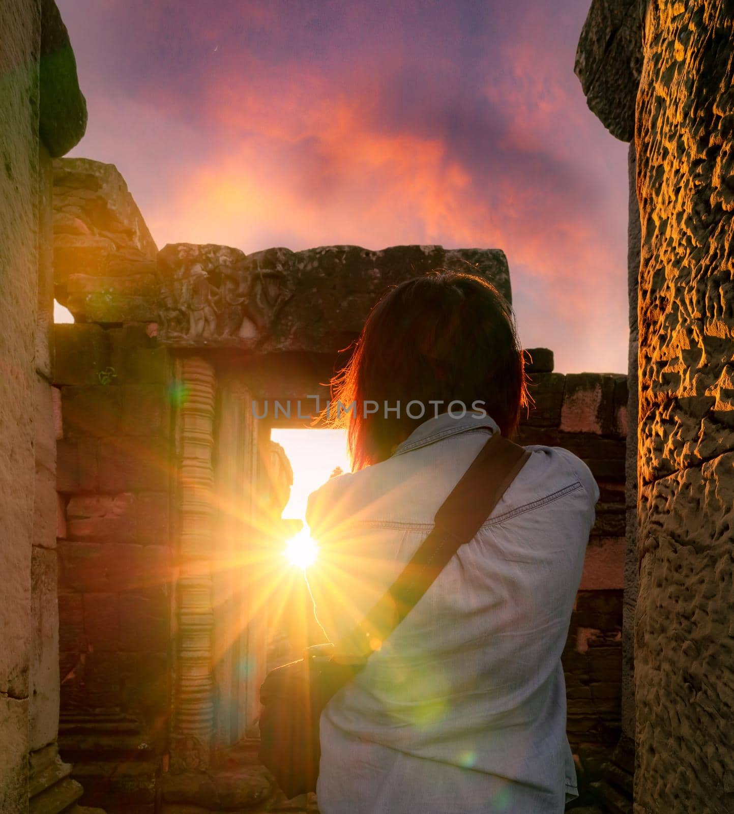 Rearview of woman photographer travel in Phimai Historical Park with sunset sky. Landmark of Nakhon Ratchasima, Thailand. Travel destinations. Historic site is ancient. Ancient building. Khmer temple. by Fahroni