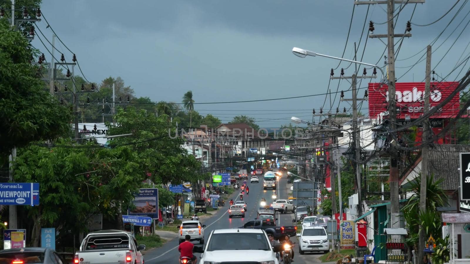 KOH SAMUI ISLAND, THAILAND - 11 JULY 2019 Busy transport populated city street in cloudy day. Typical street full of motorcycles and cars. Thick blue clouds before storm during wet season. by DogoraSun