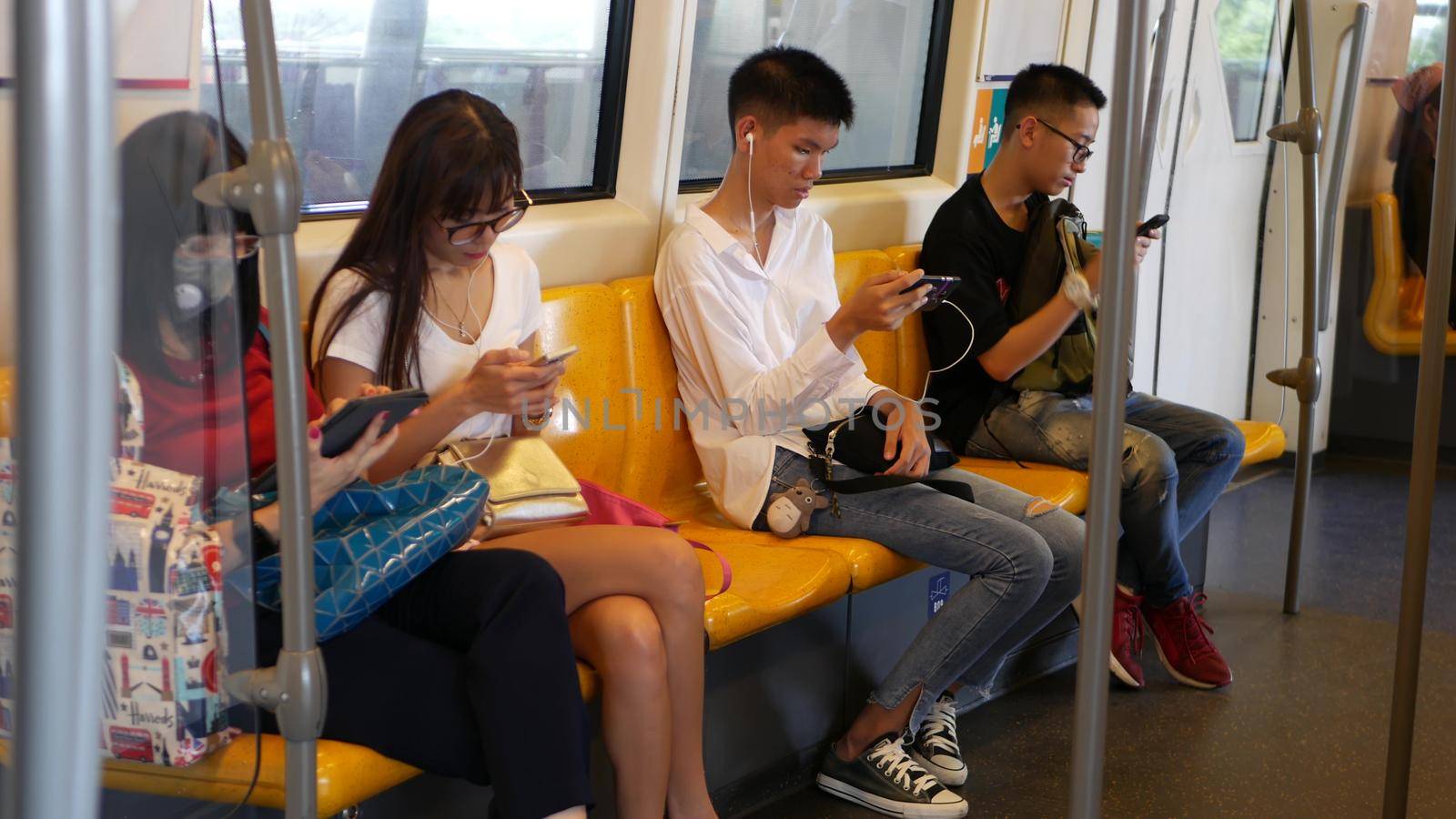 BANGKOK, THAILAND - 13 JULY, 2019: Asian passengers in train using smartphones. Thai people online surfing internet in bts car. Public transportation. Addiction from social media and phone in subway