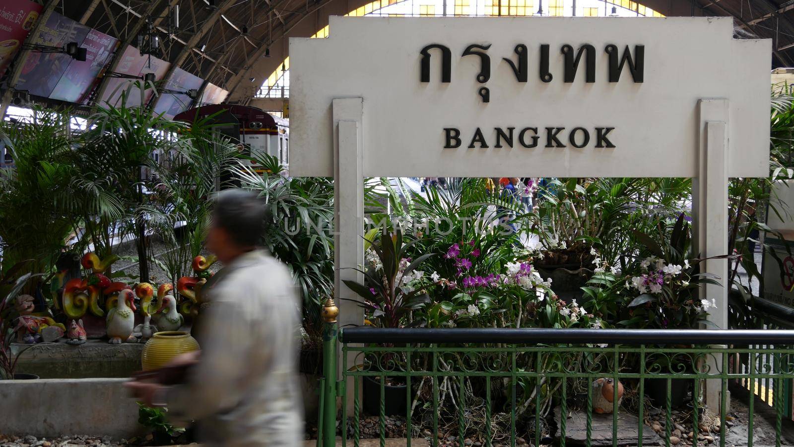 BANGKOK, THAILAND - 11 JULY, 2019: Signpost with name of city. Hua Lamphong main railroad station of state railway transport, SRT. Passengers on platform near sign board. People and trains on tracks