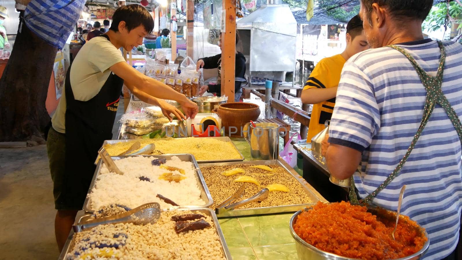 BANGKOK, THAILAND - 13 JULY 2019: Lat Mayom khlong river canal traditional classic floating market. Iconic local asian street food selling. Sellers and buyers at the counters with exotic goods.