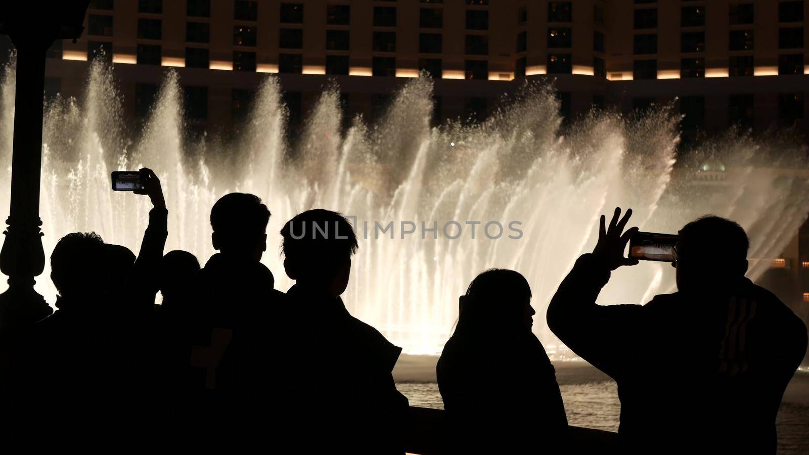 LAS VEGAS, NEVADA USA - 13 DEC 2019: People looking at Bellagio fountain musical performance at night. Contrast silhouettes and glowing dancing splashing water. Entertainment show in gambling city by DogoraSun