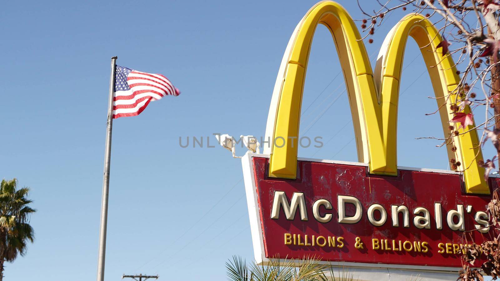 VISTA, CALIFORNIA USA - 16 FEB 2020: McDonalds logo sign and American flag. Yellow letter M icon and Stars and Stripes. Golden Arches emblem, brand sign in suburban district. Food restaurant on street