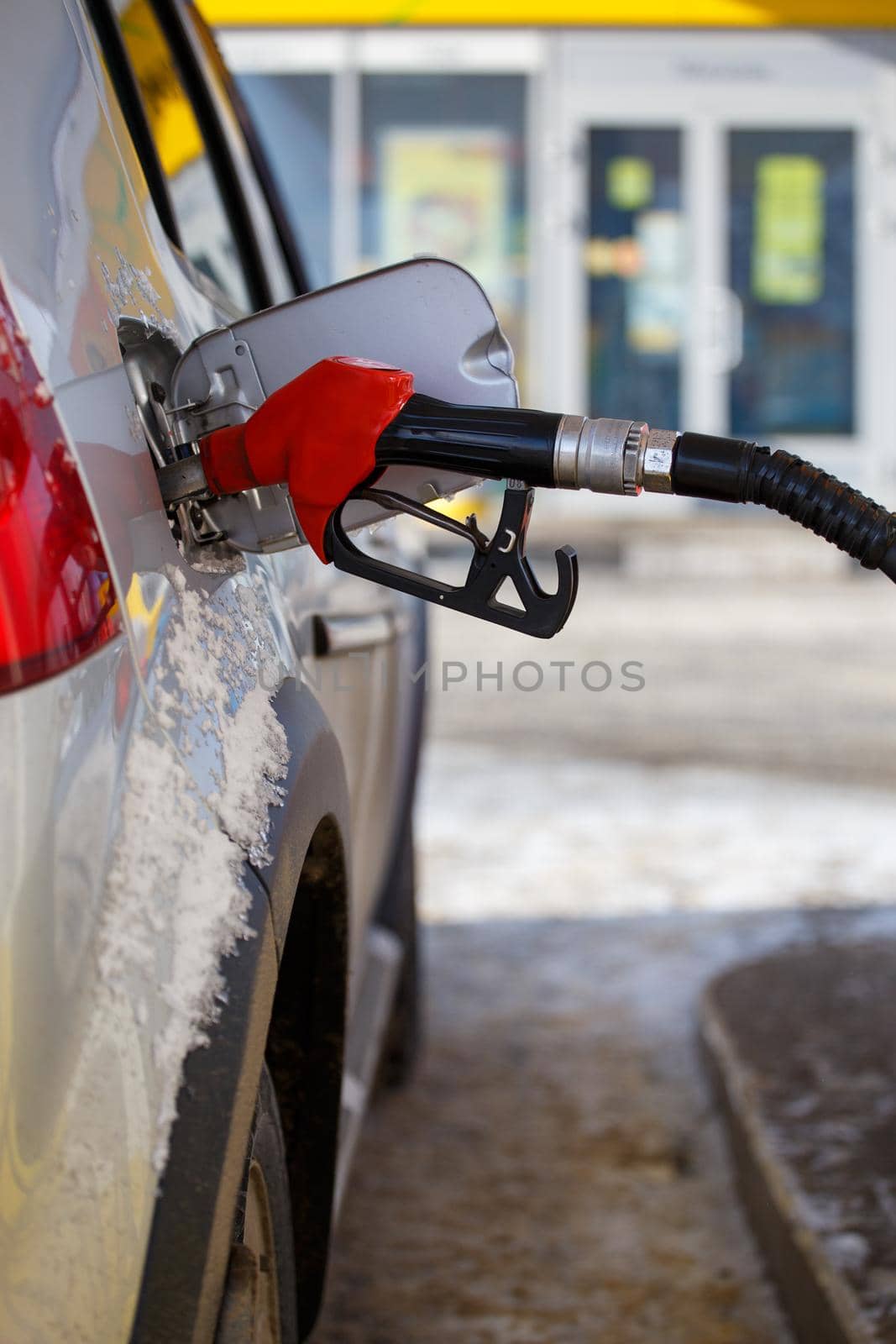 silver metallic car refueling on winter day gas station - close-up with selective focus and blurry background.