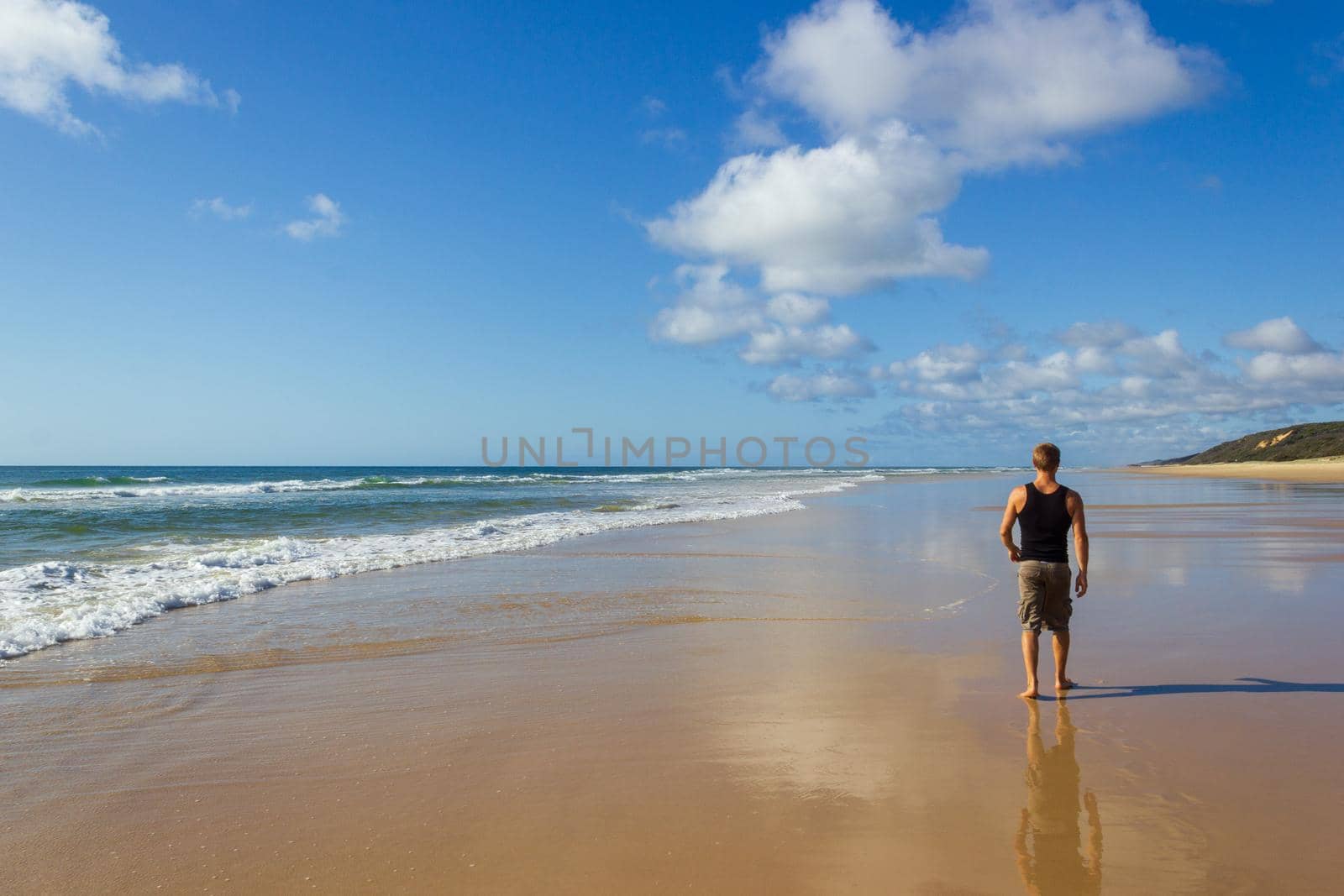 young man walking on the main transportation highway on Fraser Island - wide wet sand beach coast facing Pacific ocean - long 75 miles beach by bettercallcurry