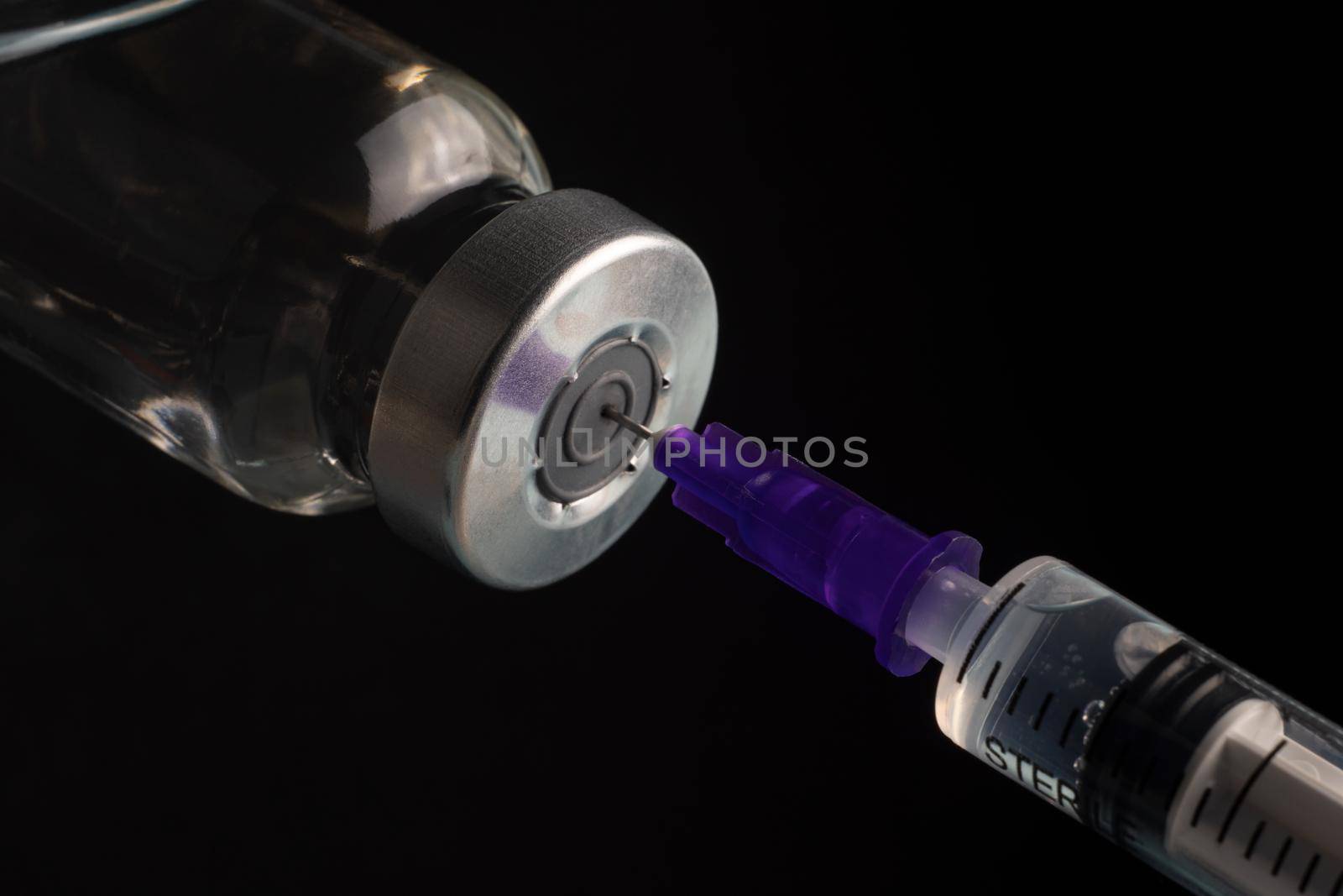 Close-up of filling a syringe with vaccine on a black background. A syringe with a needle draws the medicine. by Yurii73