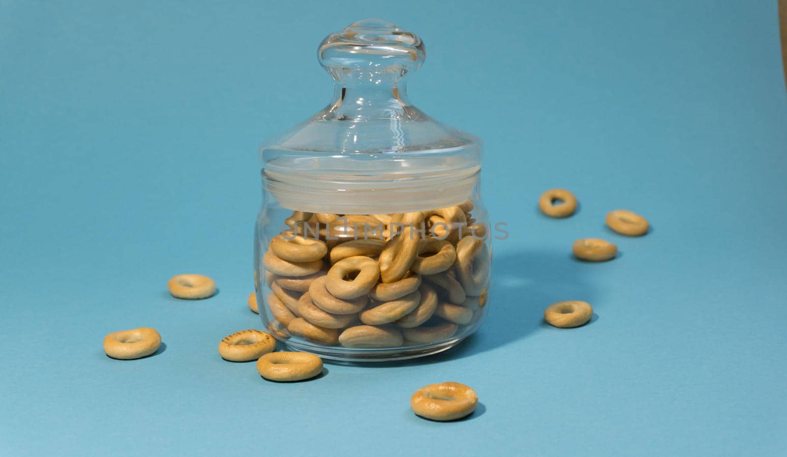 Yellow small bagels in a glass sealed container on a blue background.