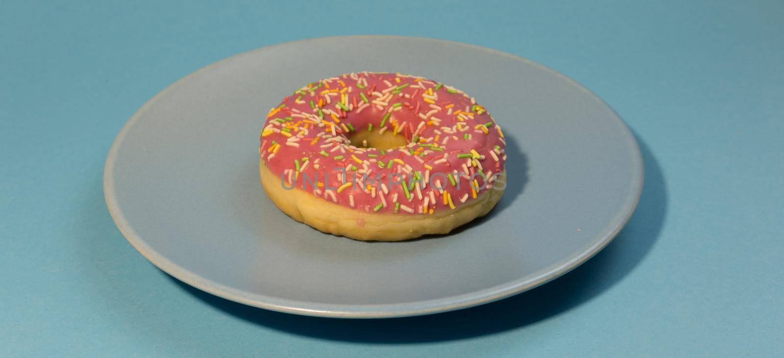 Pink sweet doughnut or donut with colored sprinkles on a blue background. Bitten off American bagel.