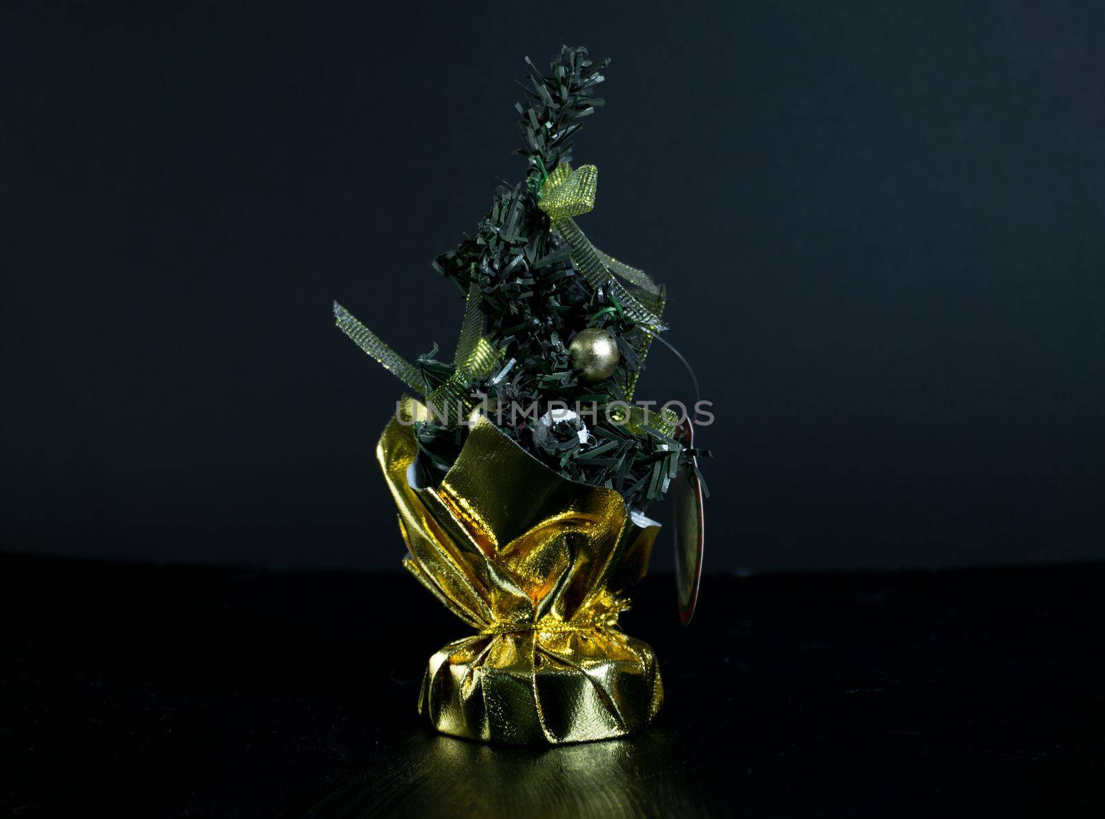 Small Christmas tree in a bag with decorations. Table accessory with gold decor. Christmas tree on black background for greeting cards