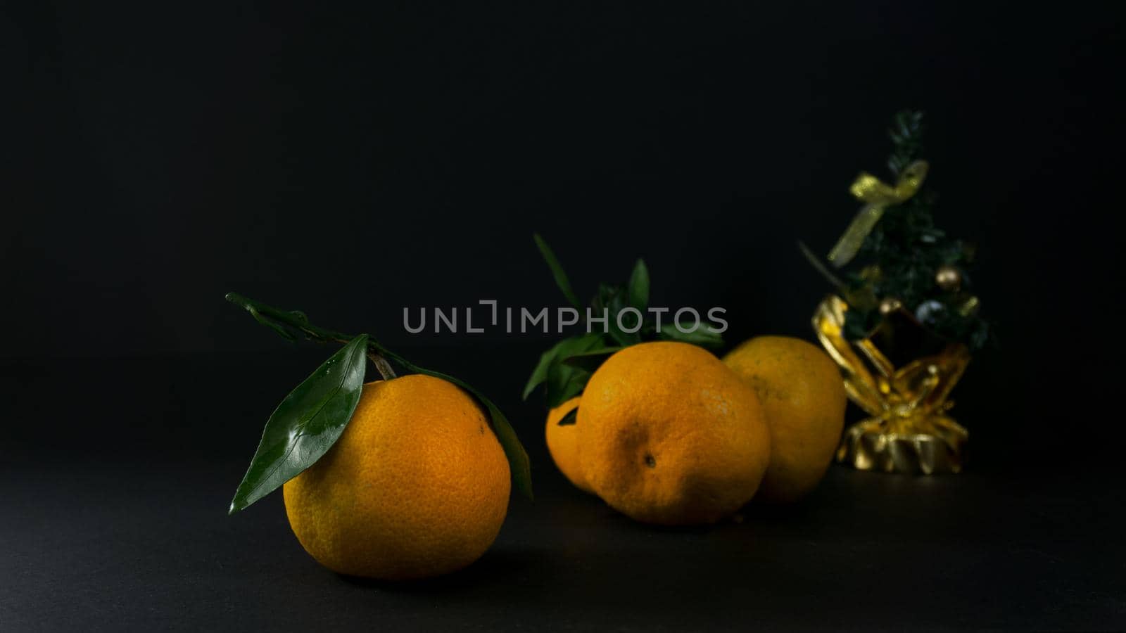 Christmas photo with a festive tree and tangerines on a dark background.