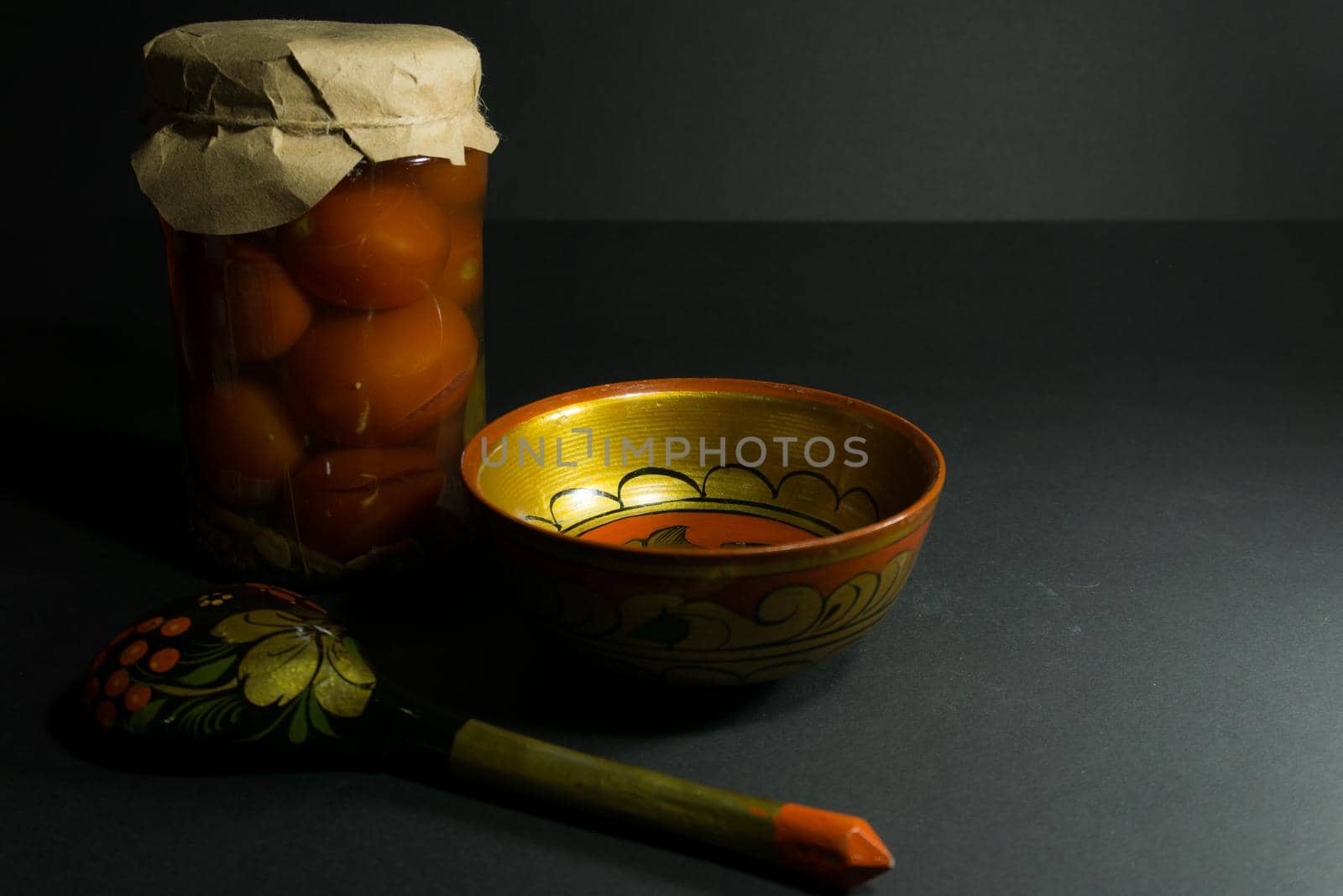 Jar of pickled tomatoes, a spoon with folk painting and a wooden bowl