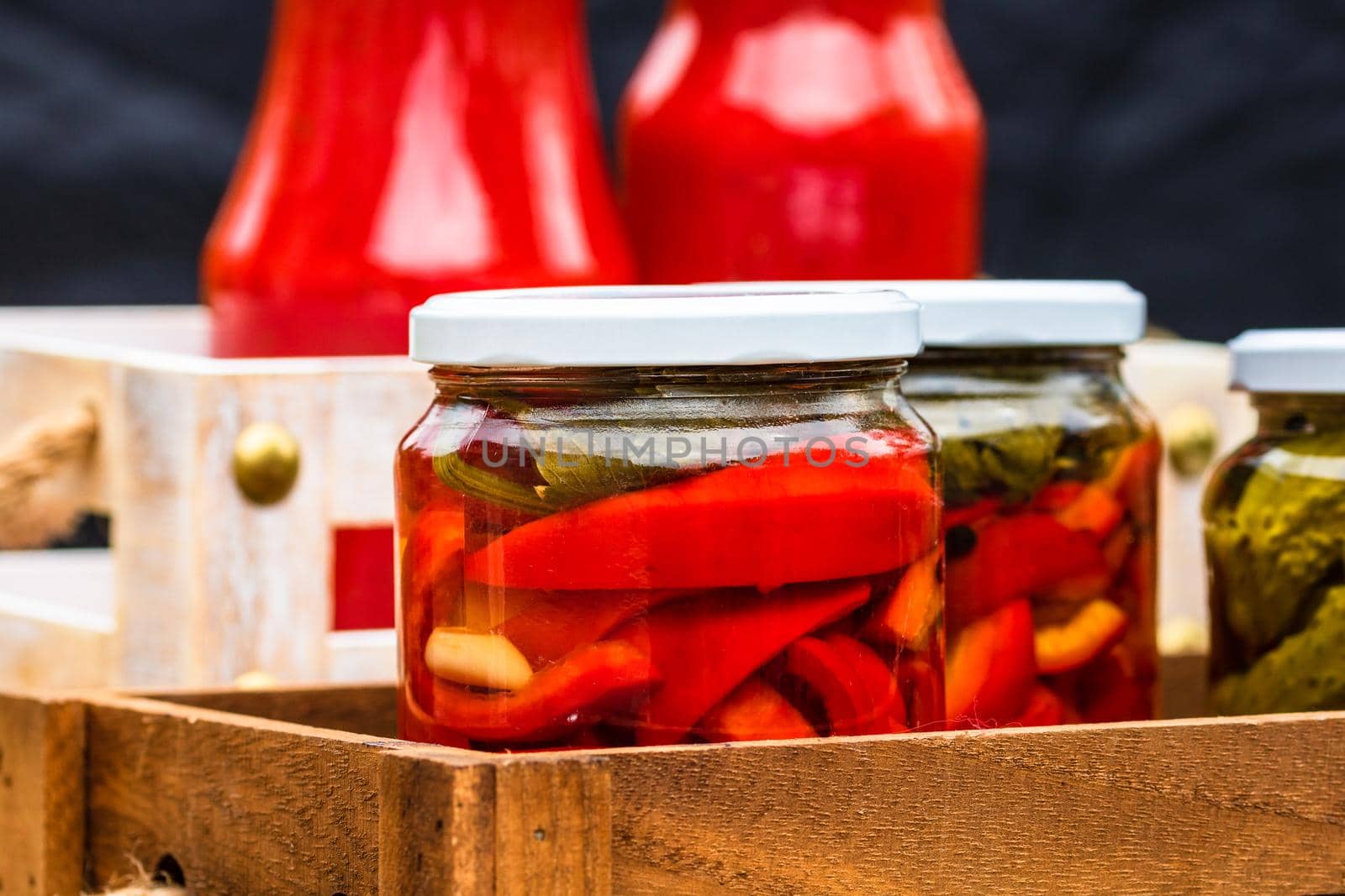 Wooden crate with glass jars with pickled red bell peppers.Preserved food concept, canned vegetables isolated in a rustic composition. by vladispas