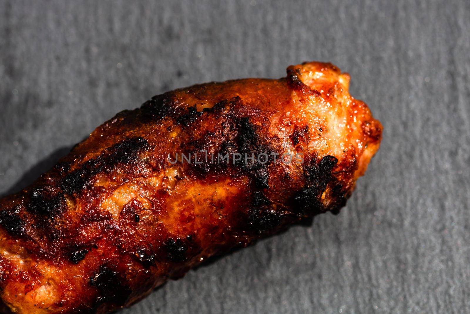 Close up of grilled sausage on small black cutting board isolated. Barbecue, grill and food concept.