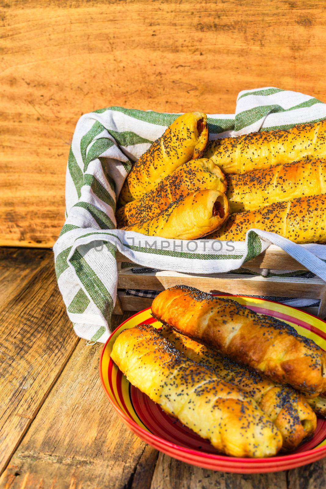 Sausages baked in dough sprinkled with salt and poppy seeds in a rustic composition. Sausages rolls, delicious homemade pastries.