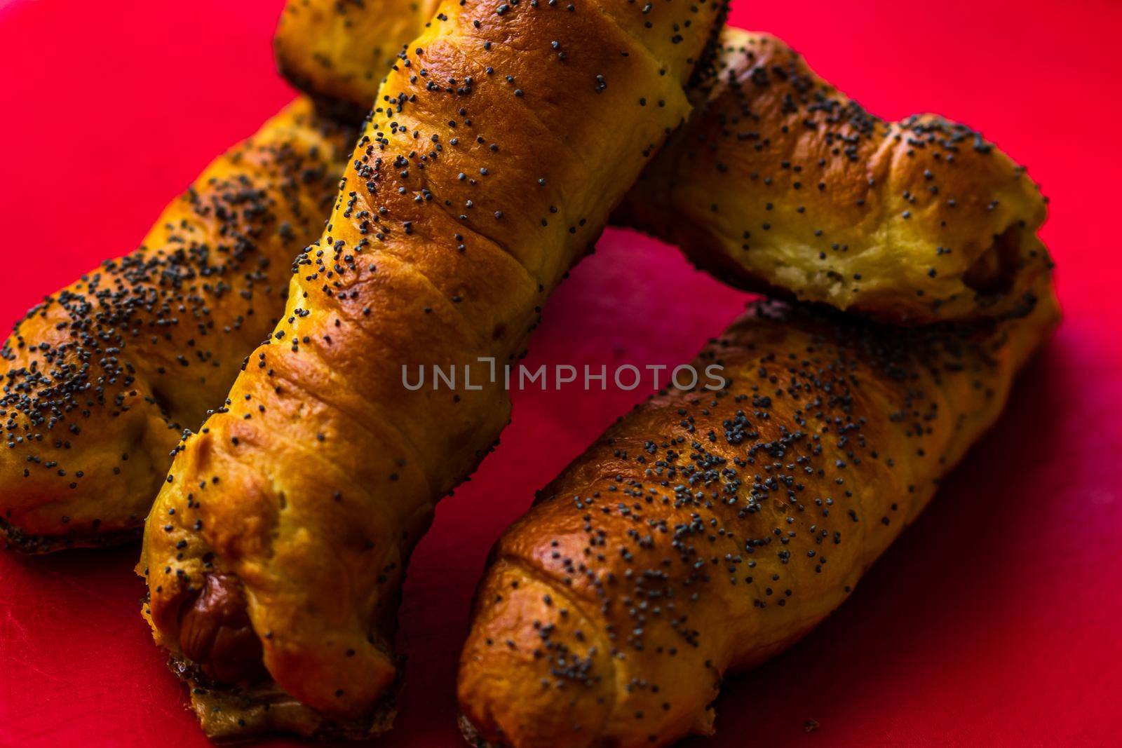 Close up of sausages baked in dough sprinkled with salt and poppy seeds. Sausages rolls, delicious homemade pastries isolated. by vladispas