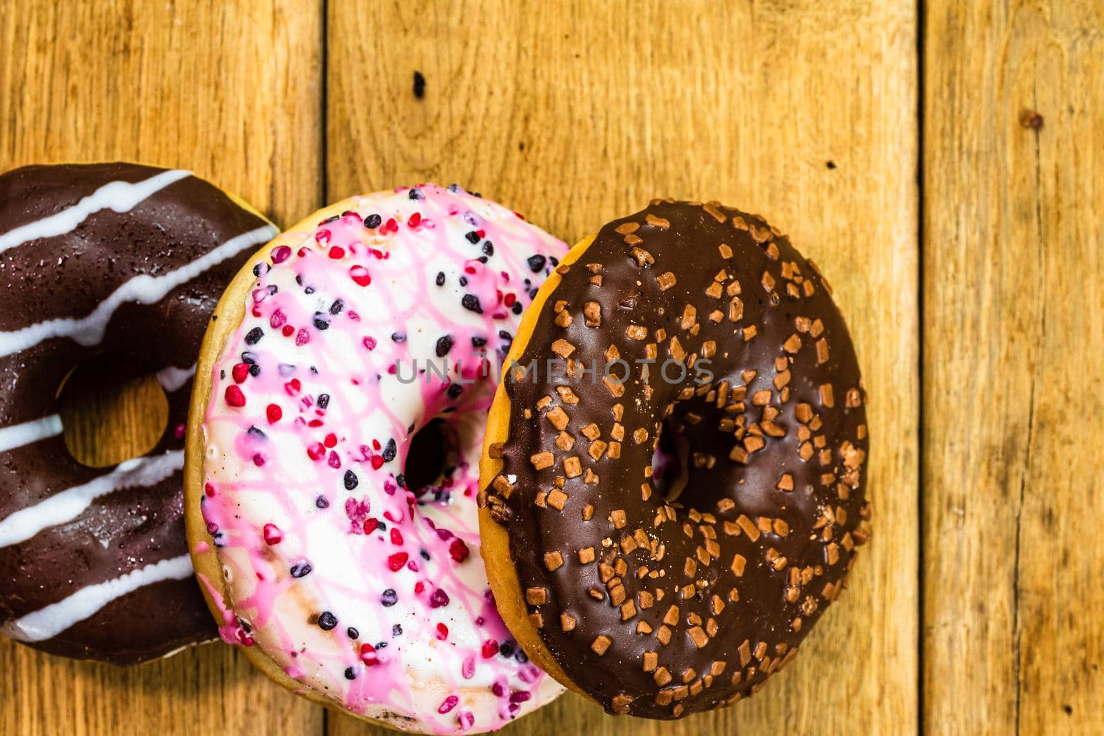 Colorful donuts on wooden table. Sweet icing sugar food with glazed sprinkles, doughnut with chocolate frosting. Top view with copy space