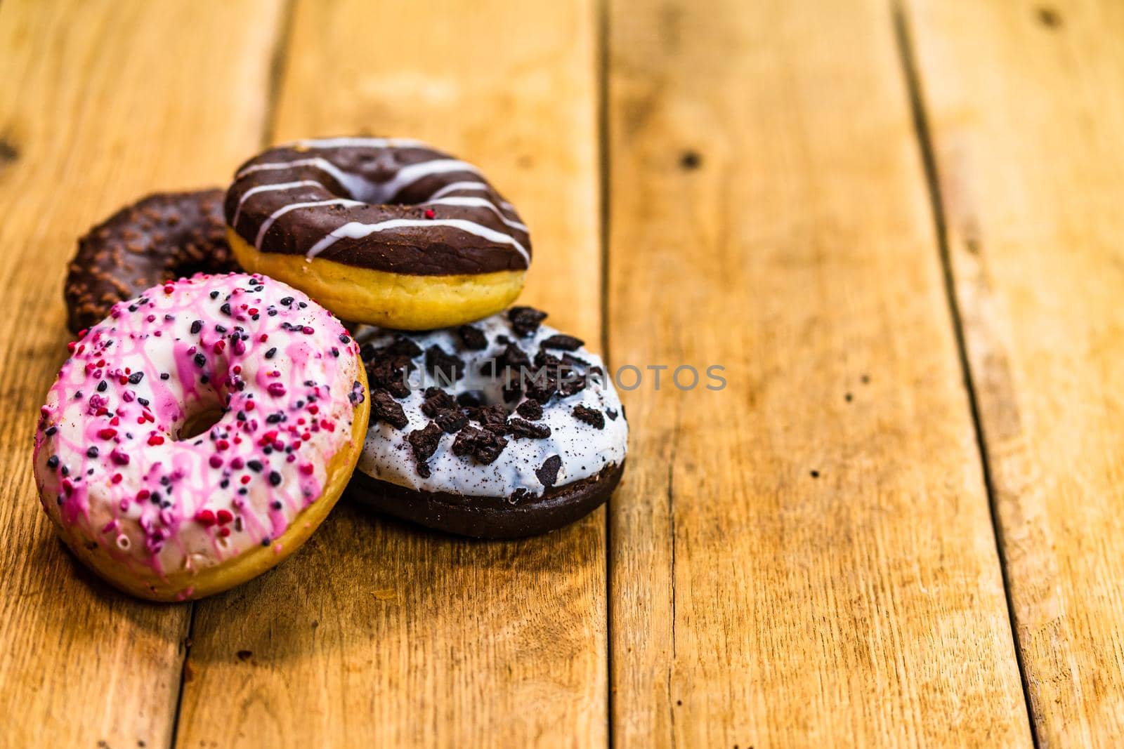 Colorful donuts on wooden table. Sweet icing sugar food with glazed sprinkles, doughnut with chocolate frosting. Top view with copy space