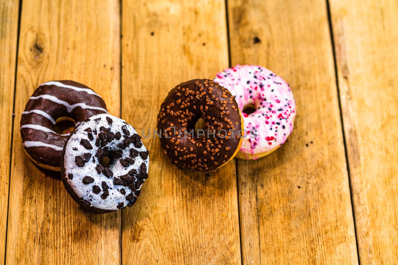 Colorful donuts on wooden table. Sweet icing sugar food with glazed sprinkles, doughnut with chocolate frosting. Top view with copy space by vladispas