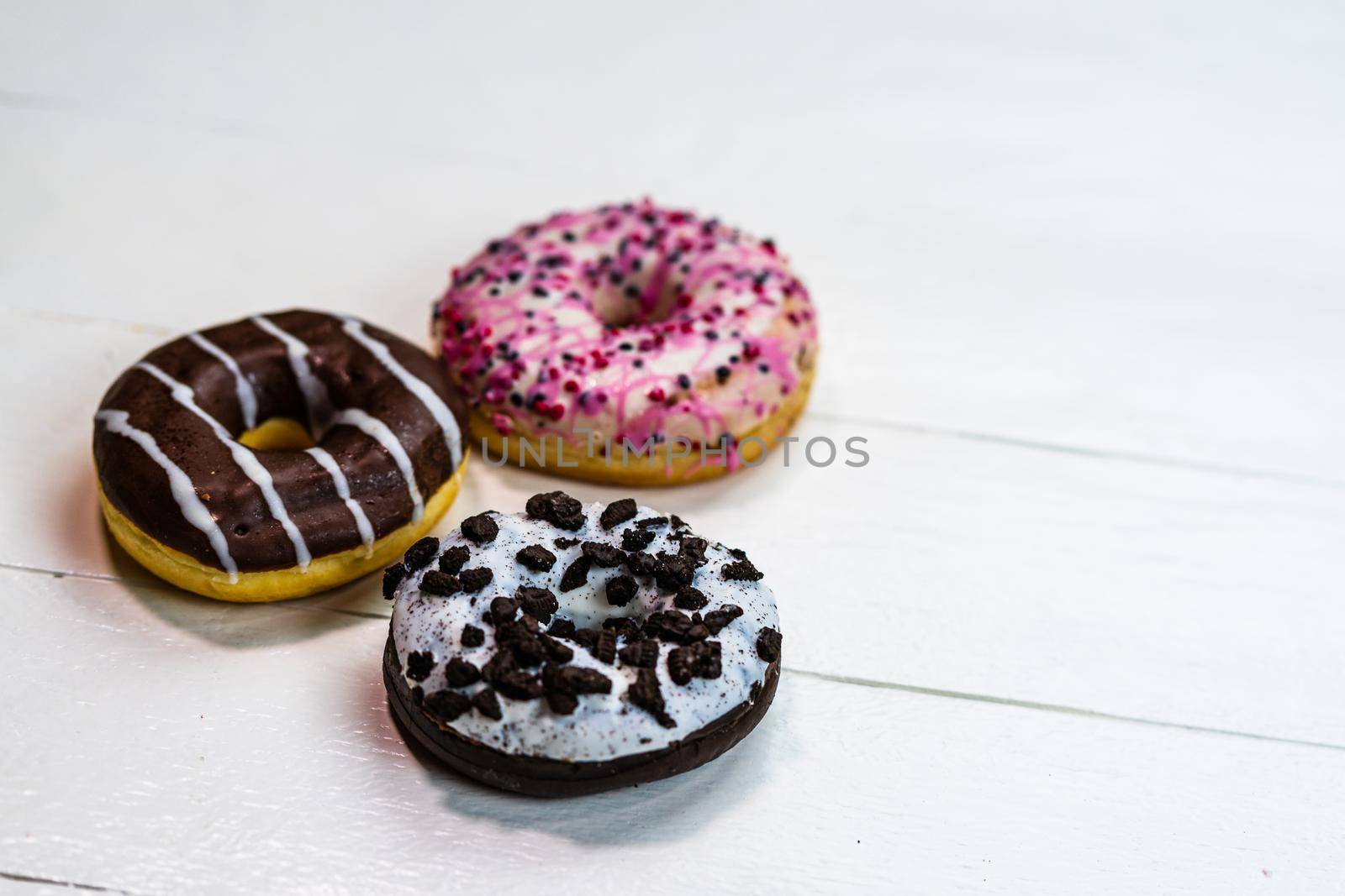 Colorful donuts on white wooden table. Sweet icing sugar food with glazed sprinkles, doughnut with frosting. Top view with copy space by vladispas