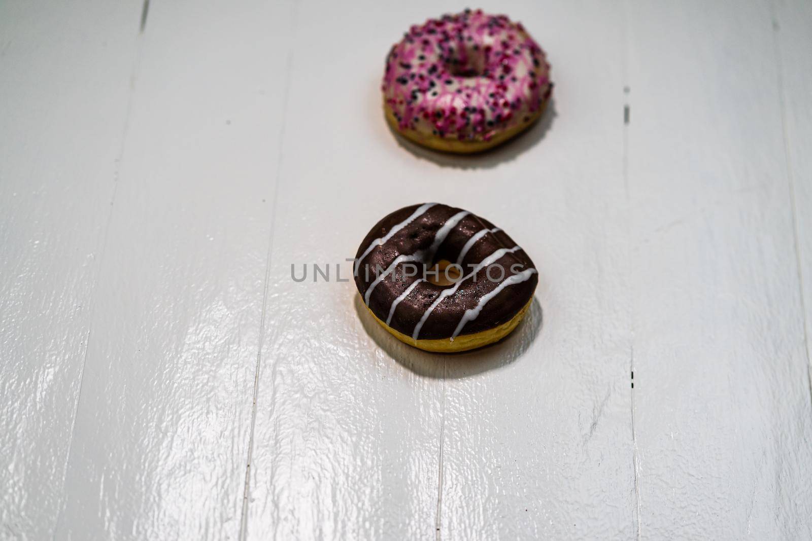 Colorful donuts on white wooden table. Sweet icing sugar food with glazed sprinkles, doughnut with frosting. Top view with copy space by vladispas