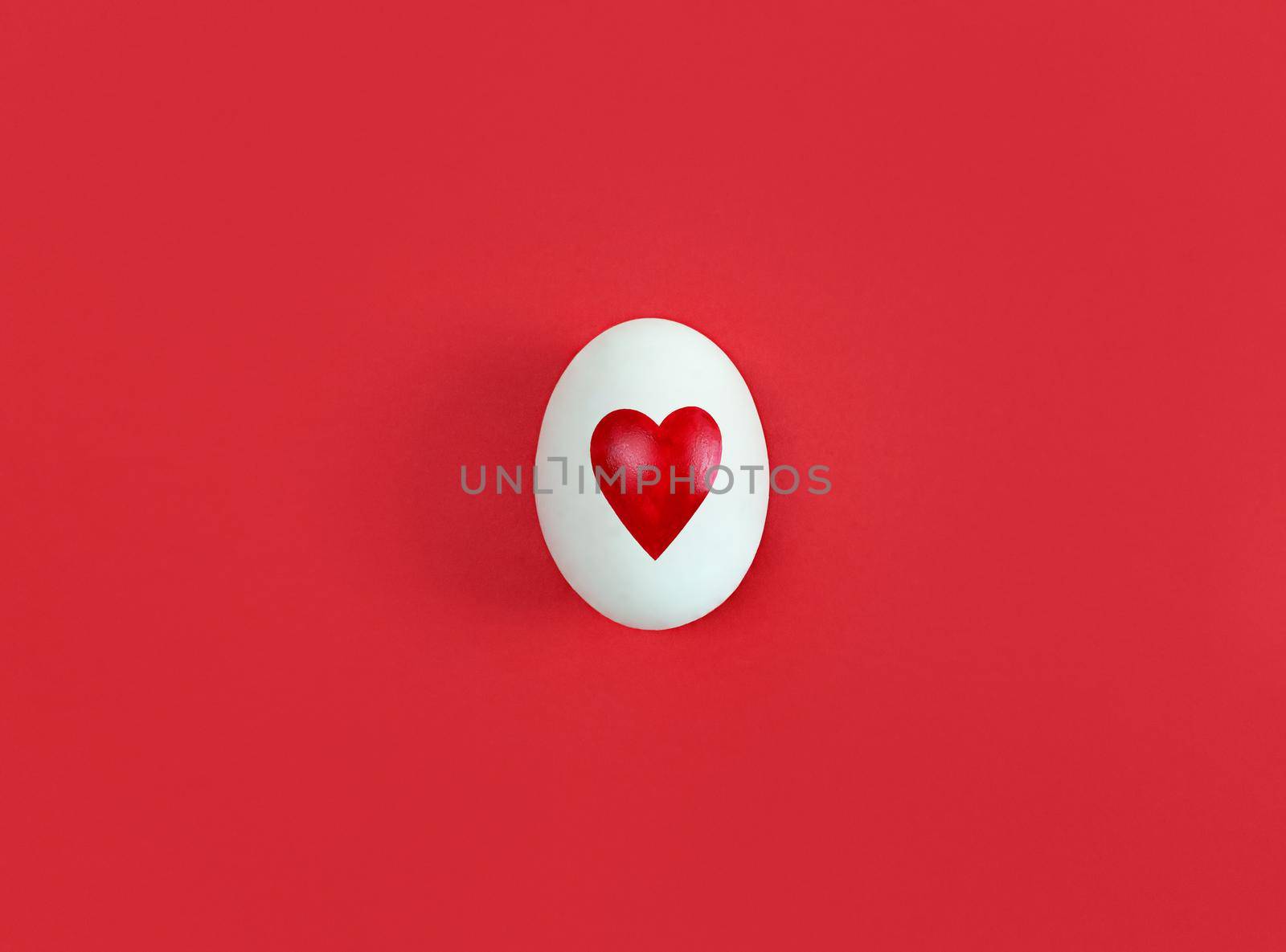 White egg with heart shape on a red background.