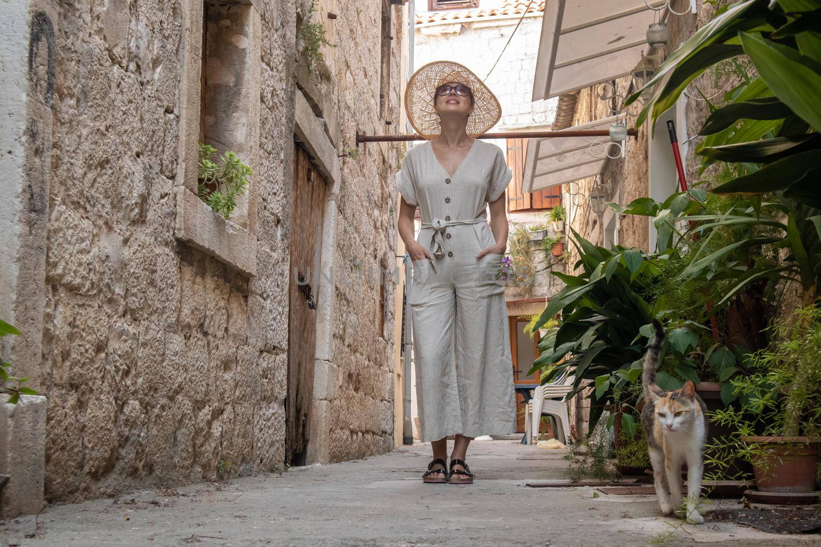 Beautiful blonde young female traveler wearing straw sun hat sightseeing and enjoying summer vacation in an old traditional costal town at Adriatic cost, Croatia.