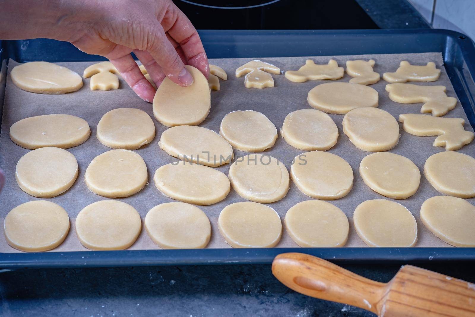  Woman prepares butter cookies at home in the kitchen, the table is sprinkled with flour, rolls out the dough, cuts out the shape, the concept of cooking festive food, christmas or easter sweets