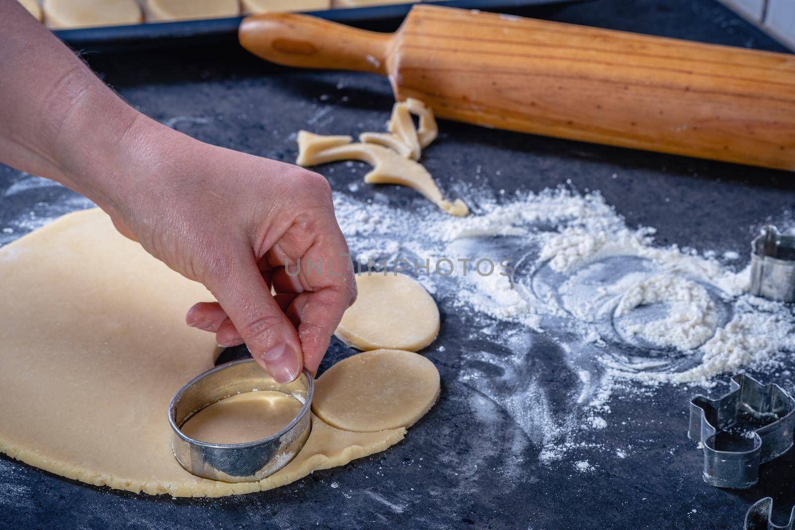  Woman prepares butter cookies at home in the kitchen, the table is sprinkled with flour, rolls out the dough, cuts out the shape, the concept of cooking festive food, christmas or easter sweets